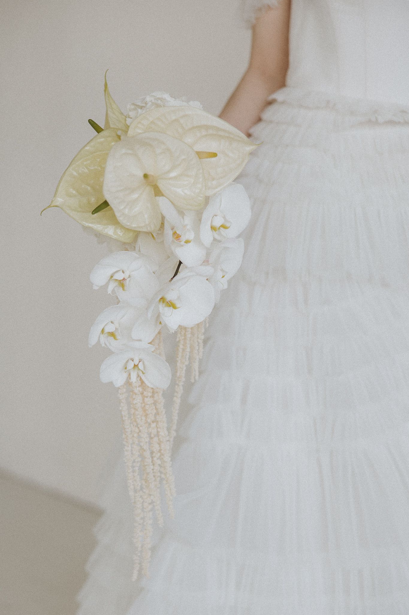 Elegant white orchid and cascading pearl wedding bouquet details shown in multiple angles against soft fabric background.