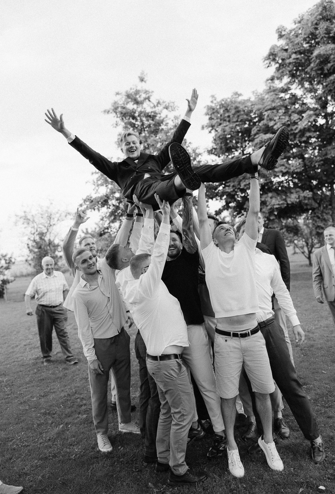 A joyful group in white and khaki raise their arms in celebration outdoors.