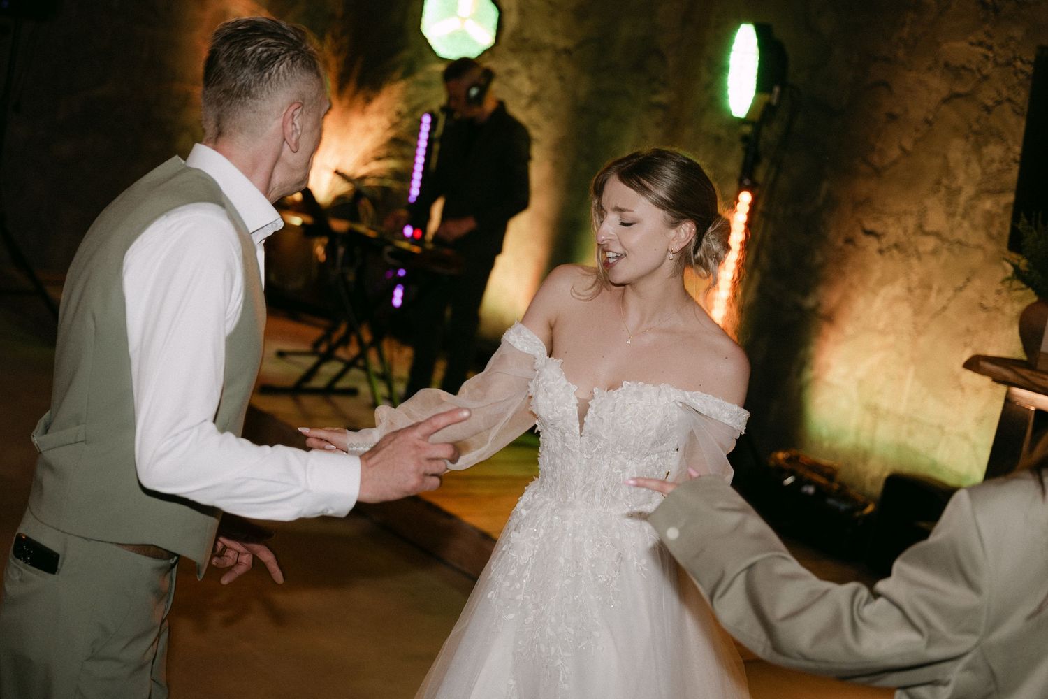 Bride in strapless beaded gown dances with groom in tan suit at cave wedding reception.