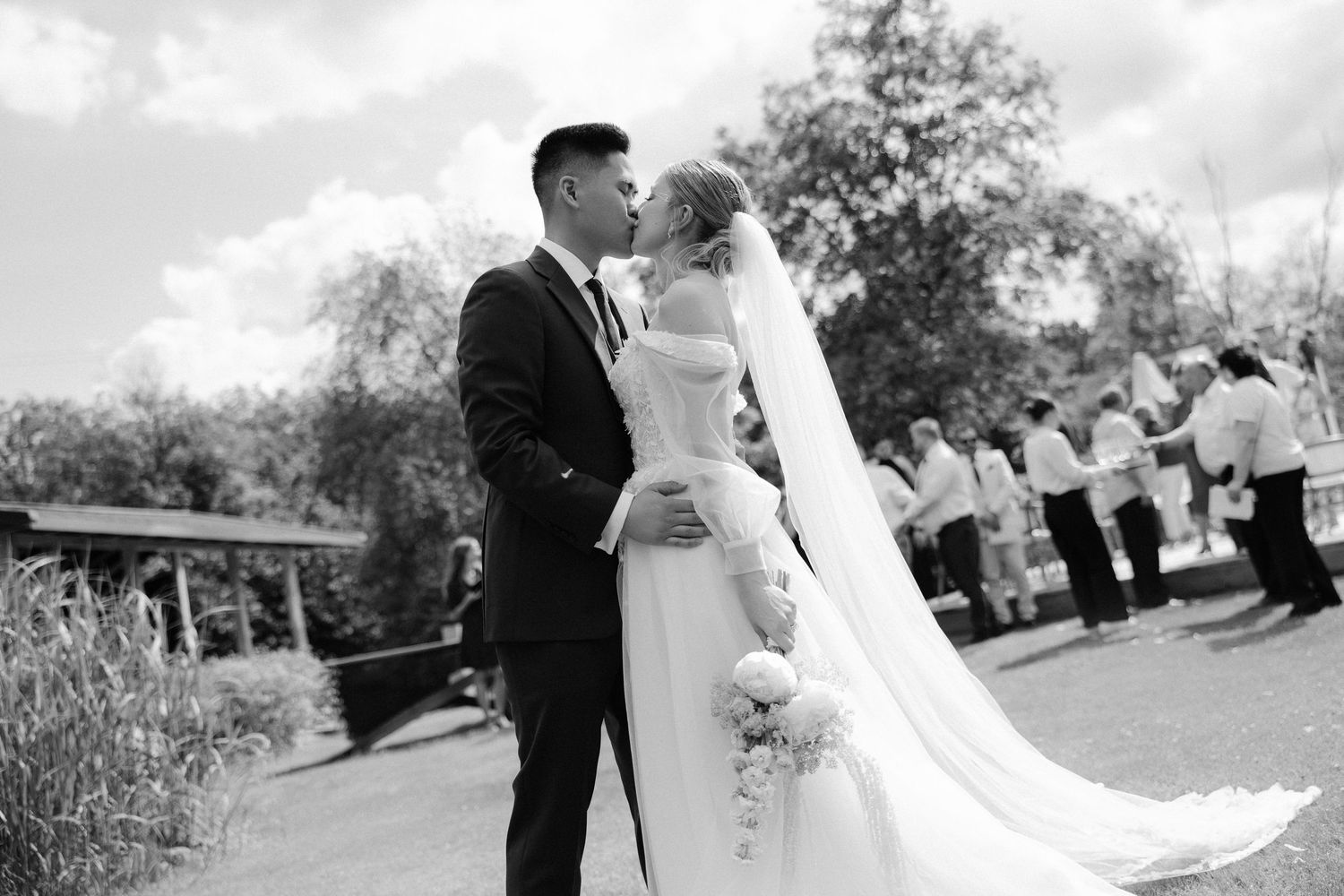 Black and white wedding photo of bride and groom sharing a romantic kiss outdoors on their wedding day.