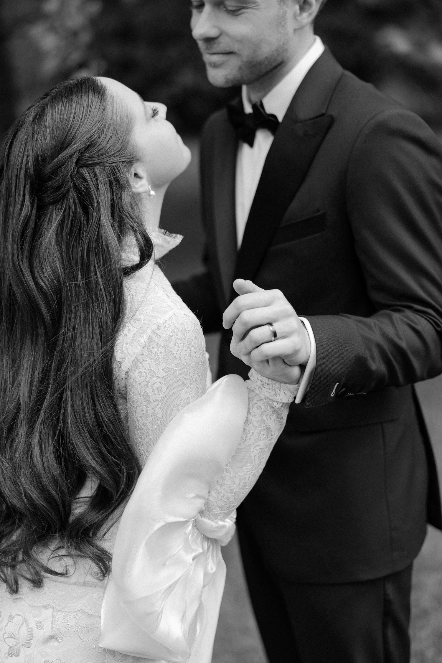 Black and white portrait of bride and groom holding hands, bride gazing up at smiling groom tenderly.