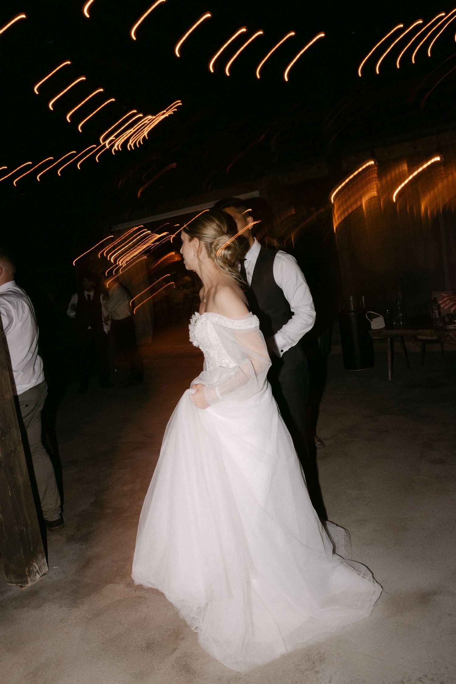 Bride and groom sharing romantic first dance under glowing lights at evening wedding reception.