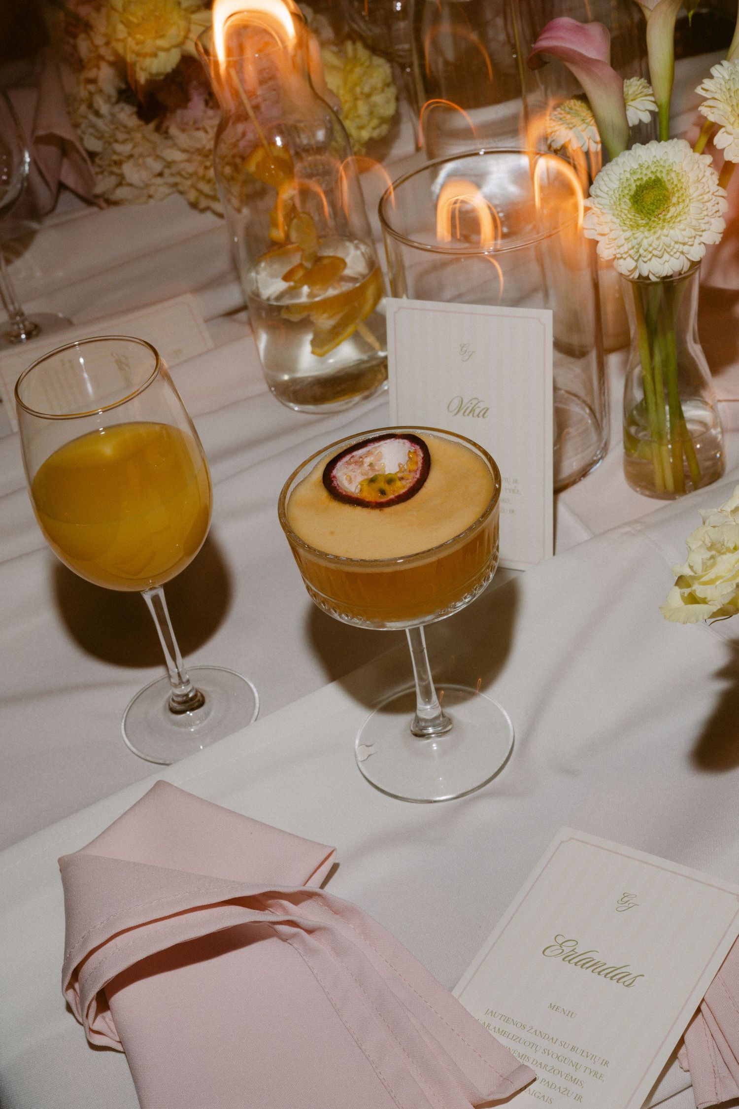 Elegant wedding reception table with cocktails, candles, pink napkins, and floral arrangements.