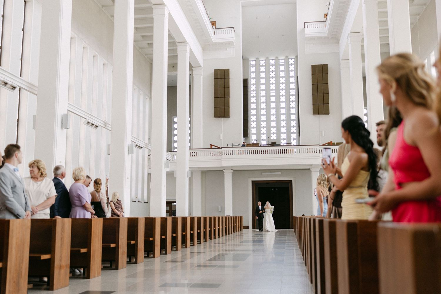 Wide shot of a church wedding ceremony with guests seated in wooden pews as the bride walks the aisle.