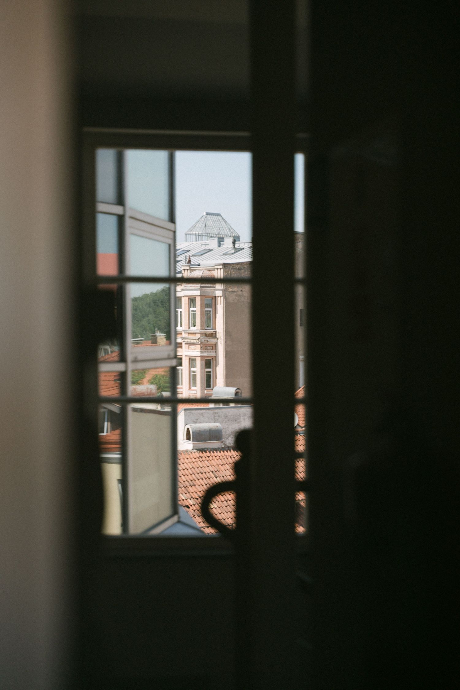 View through a dark window frame overlooking European rooftops and historic buildings on a sunny day.