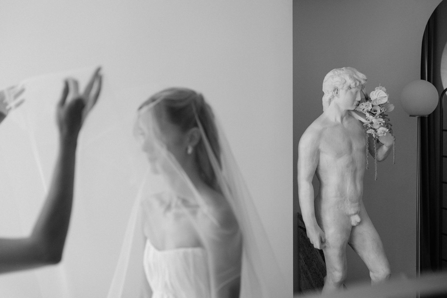 Black and white wedding photo of bride in veil beside classical male statue holding flowers.
