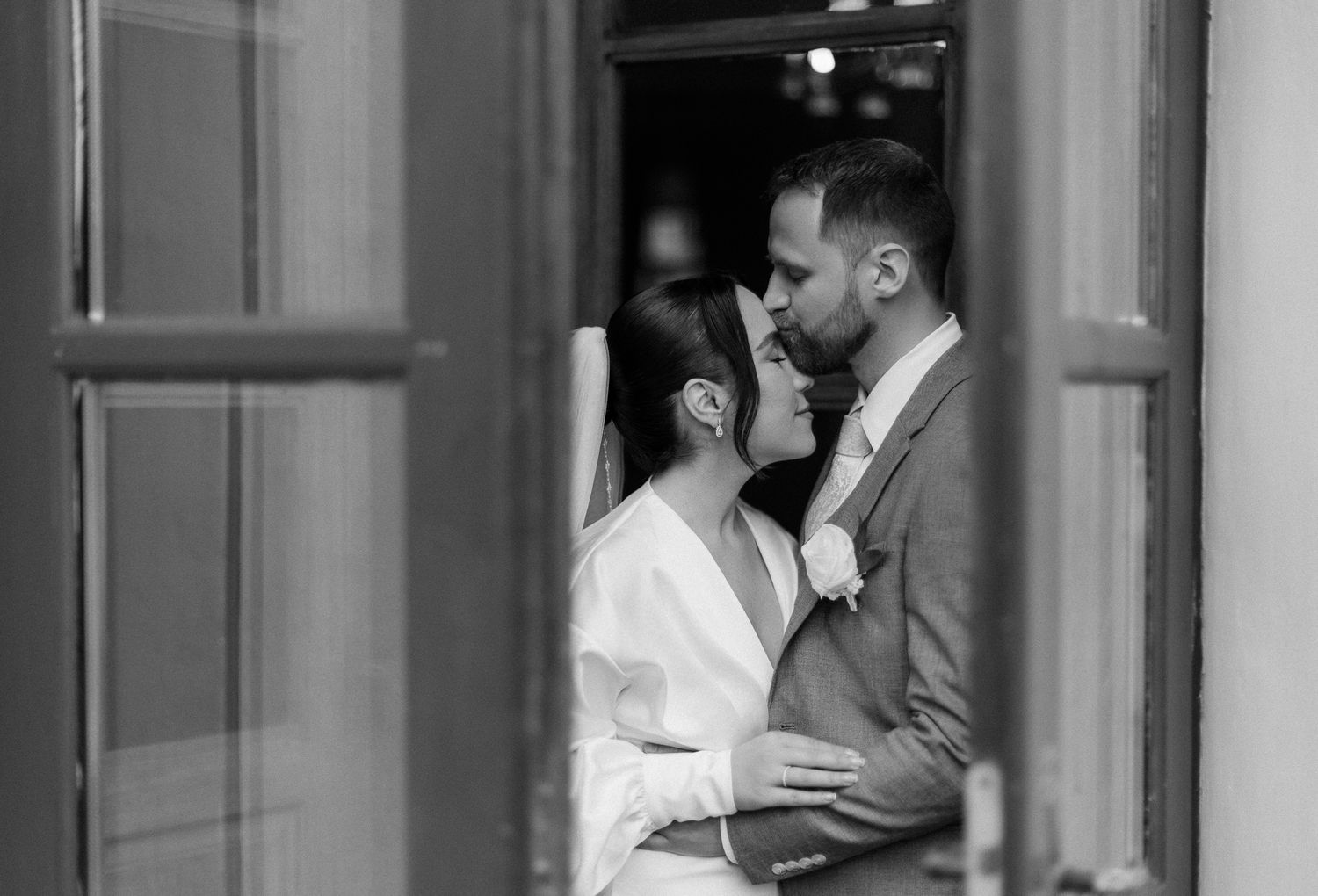 A romantic black and white photograph of a couple sharing an intimate moment through a window reflection.
