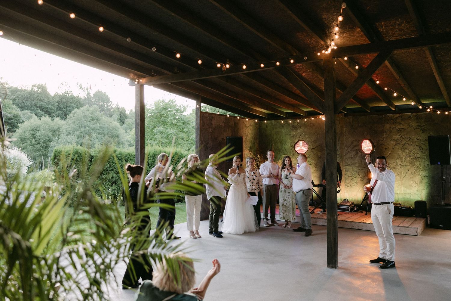 Wedding reception under covered outdoor patio with string lights, guests mingling with bride and groom.