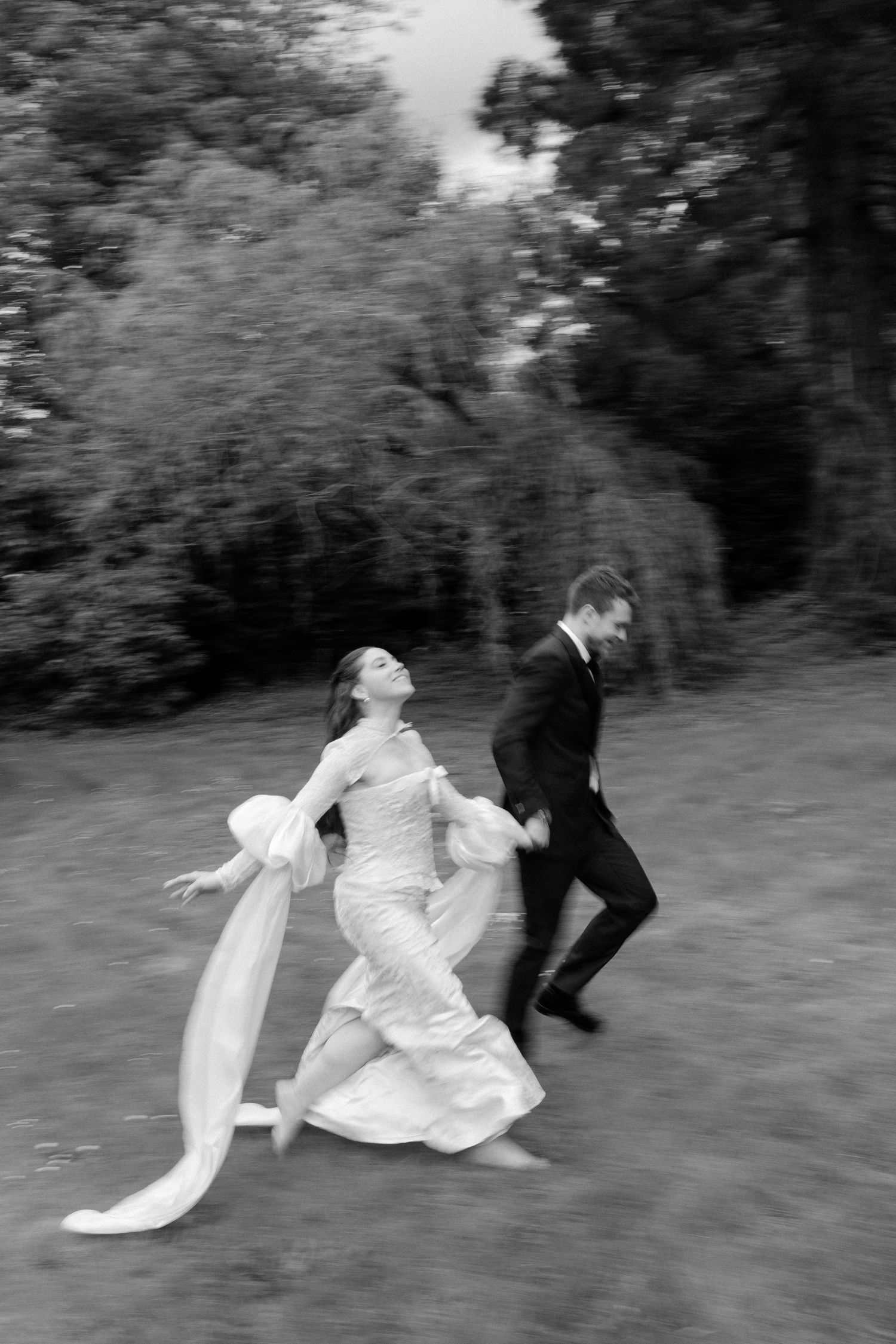 Artistic blurred black and white photo of bride and groom running joyfully through a garden.