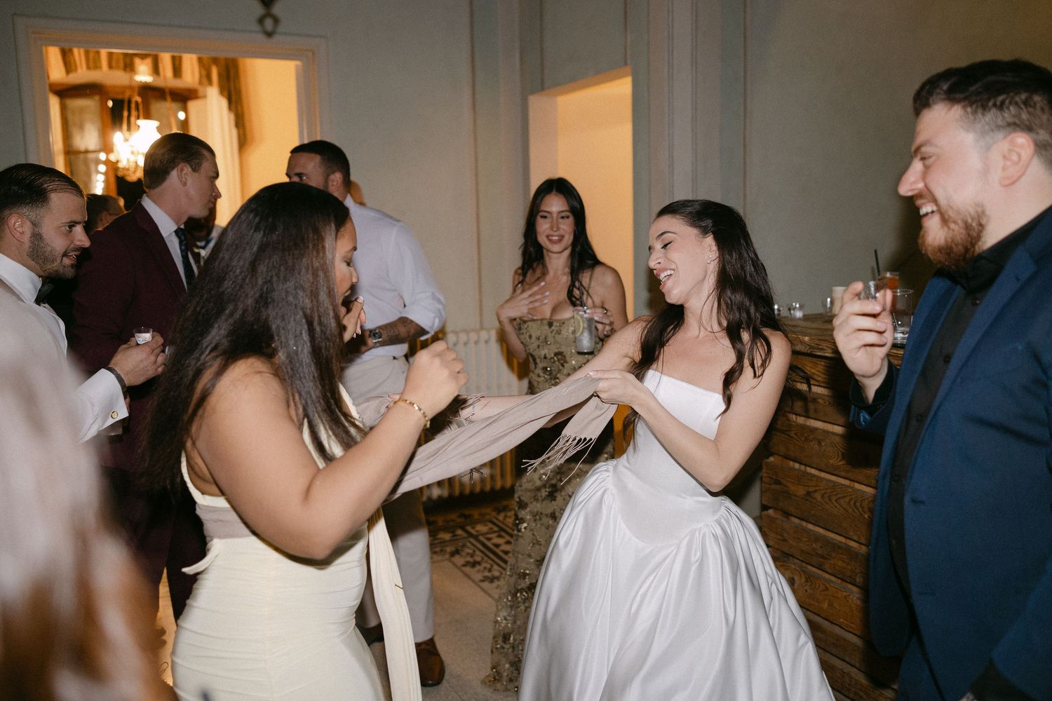 Bride dancing joyfully with a guest during a lively indoor wedding reception celebration.