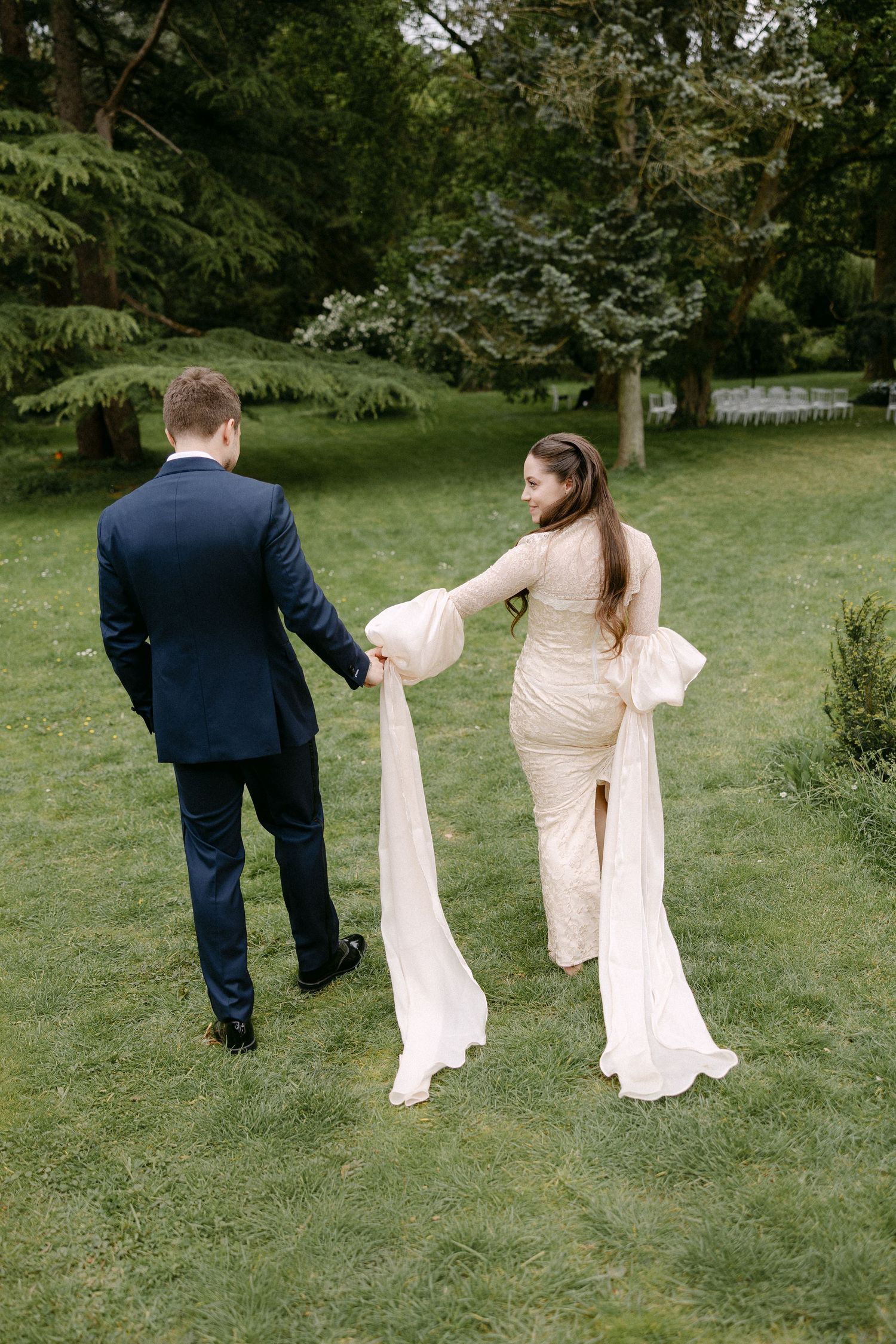 Bride and groom walking hand in hand through lush green garden grounds at their wedding venue.