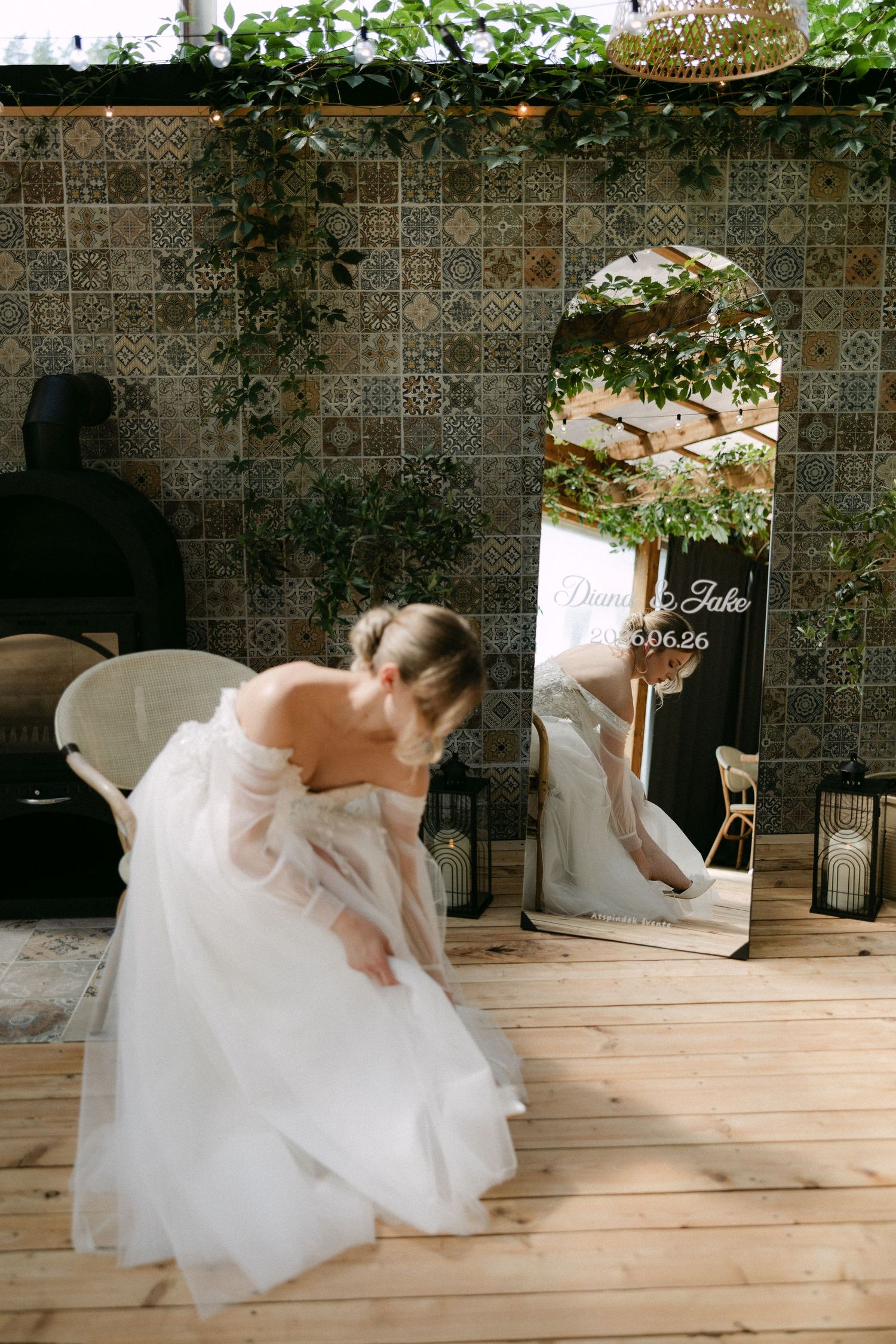 Bride in a flowing white off-shoulder gown adjusting her dress near a decorative mirror at a wedding venue.