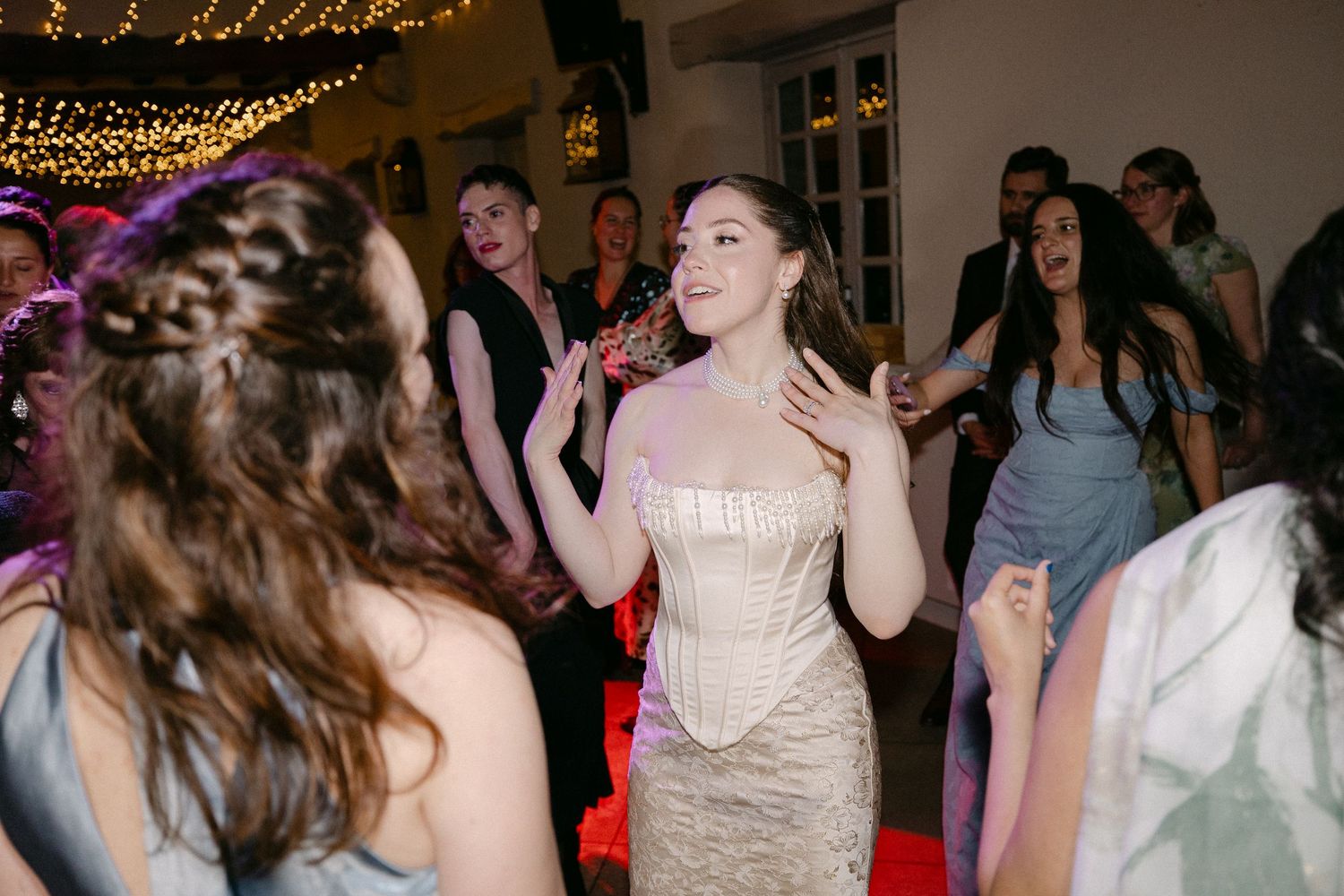 Bride in strapless lace gown dancing joyfully with guests at energetic evening wedding reception party.