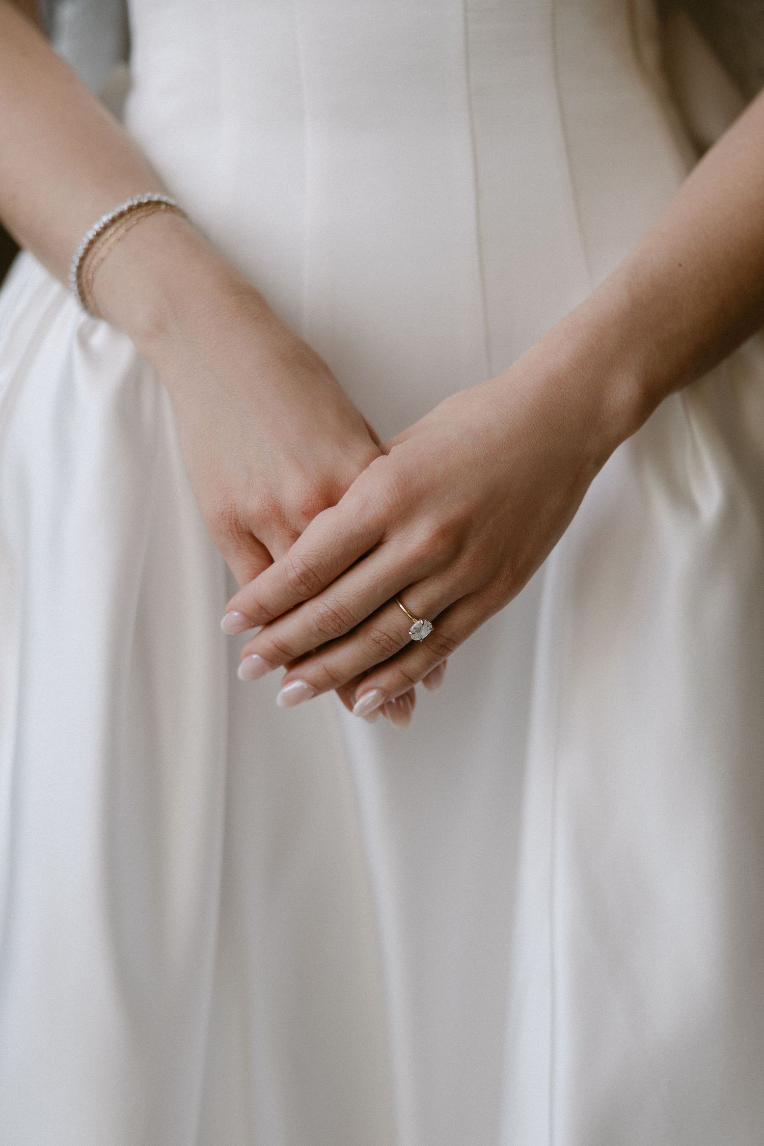 Close-up of bride's hands clasped together showing stunning solitaire diamond engagement ring and pearl bracelet.