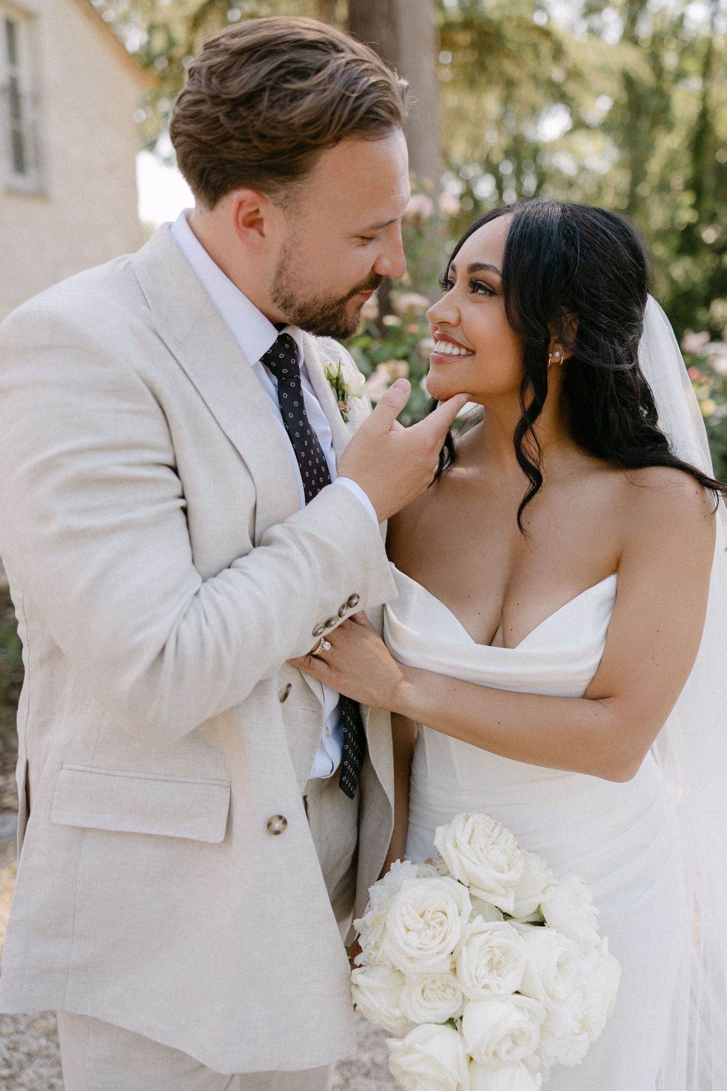 Romantic bride and groom portrait, groom tenderly touching brides face, she holds white roses.