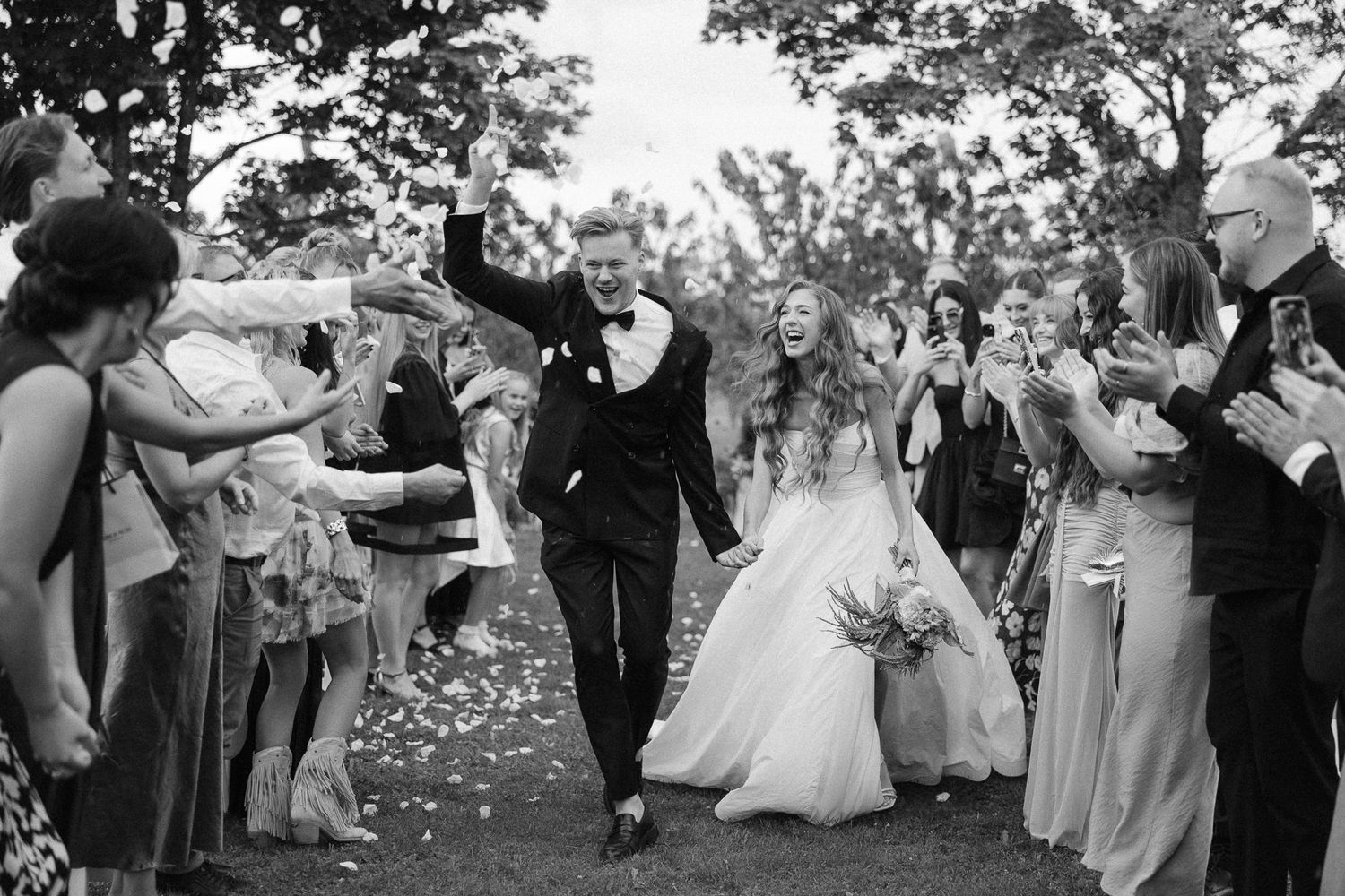 Wedding guests gather outdoors in a garden setting during a celebratory reception.