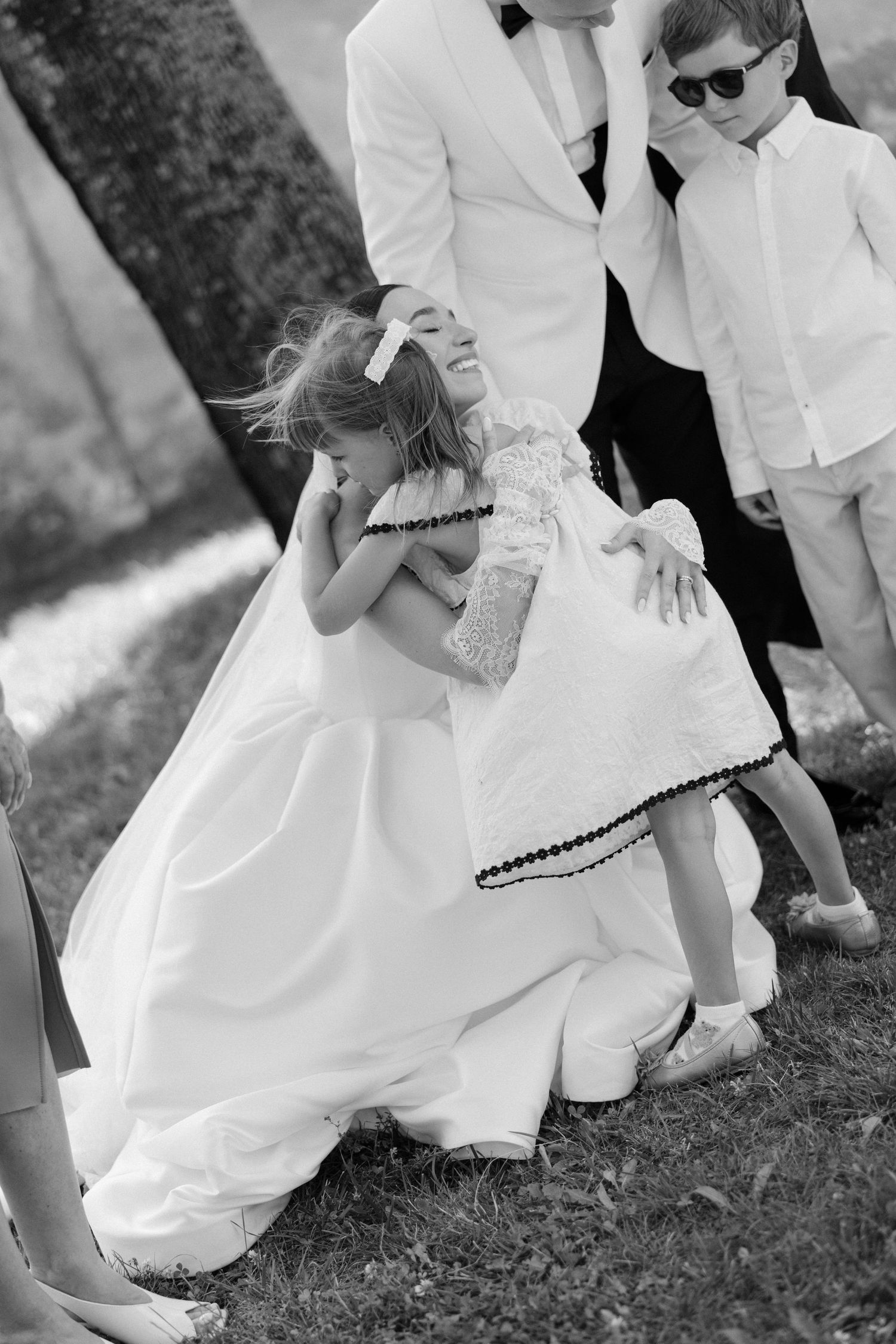 Black and white photo of a bride hugging a young flower girl at a wedding outdoor ceremony.