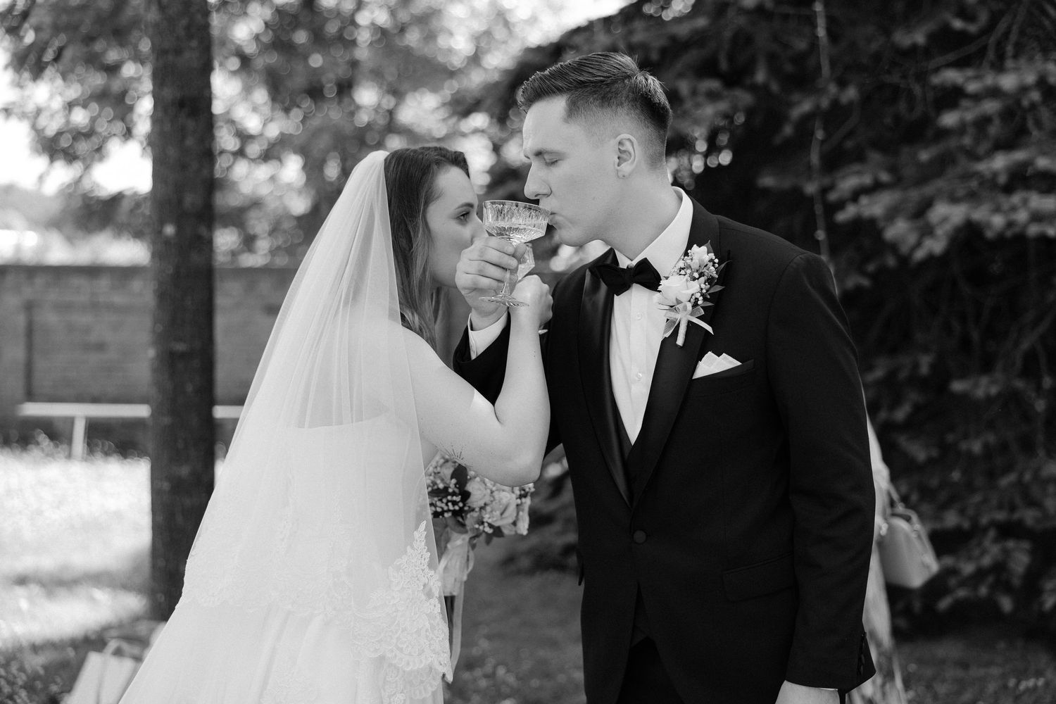 Black and white photo of a bride and groom toasting with champagne glasses on their wedding day.