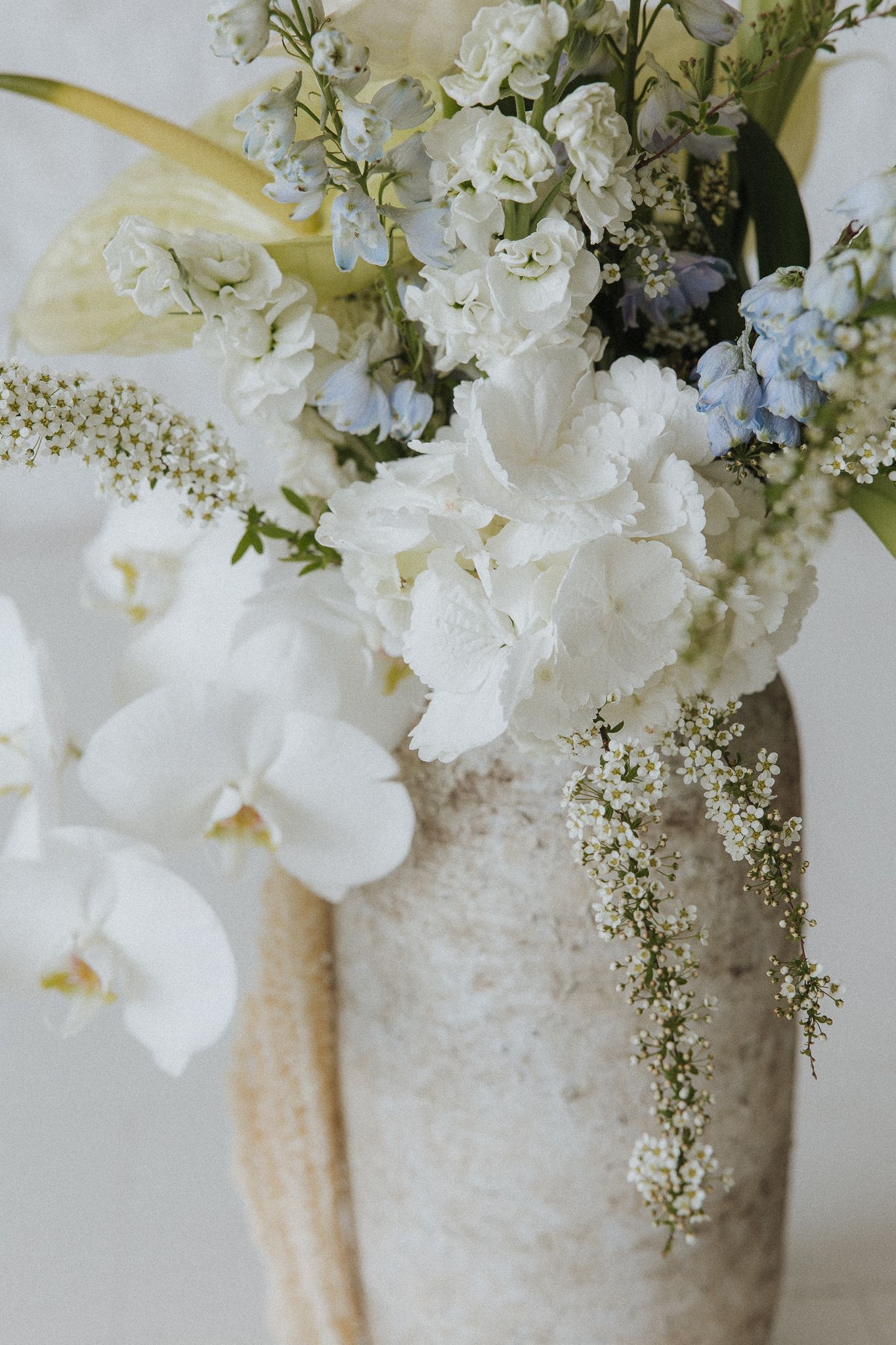 White orchids and delicate flowers arranged in textured ceramic vase.
