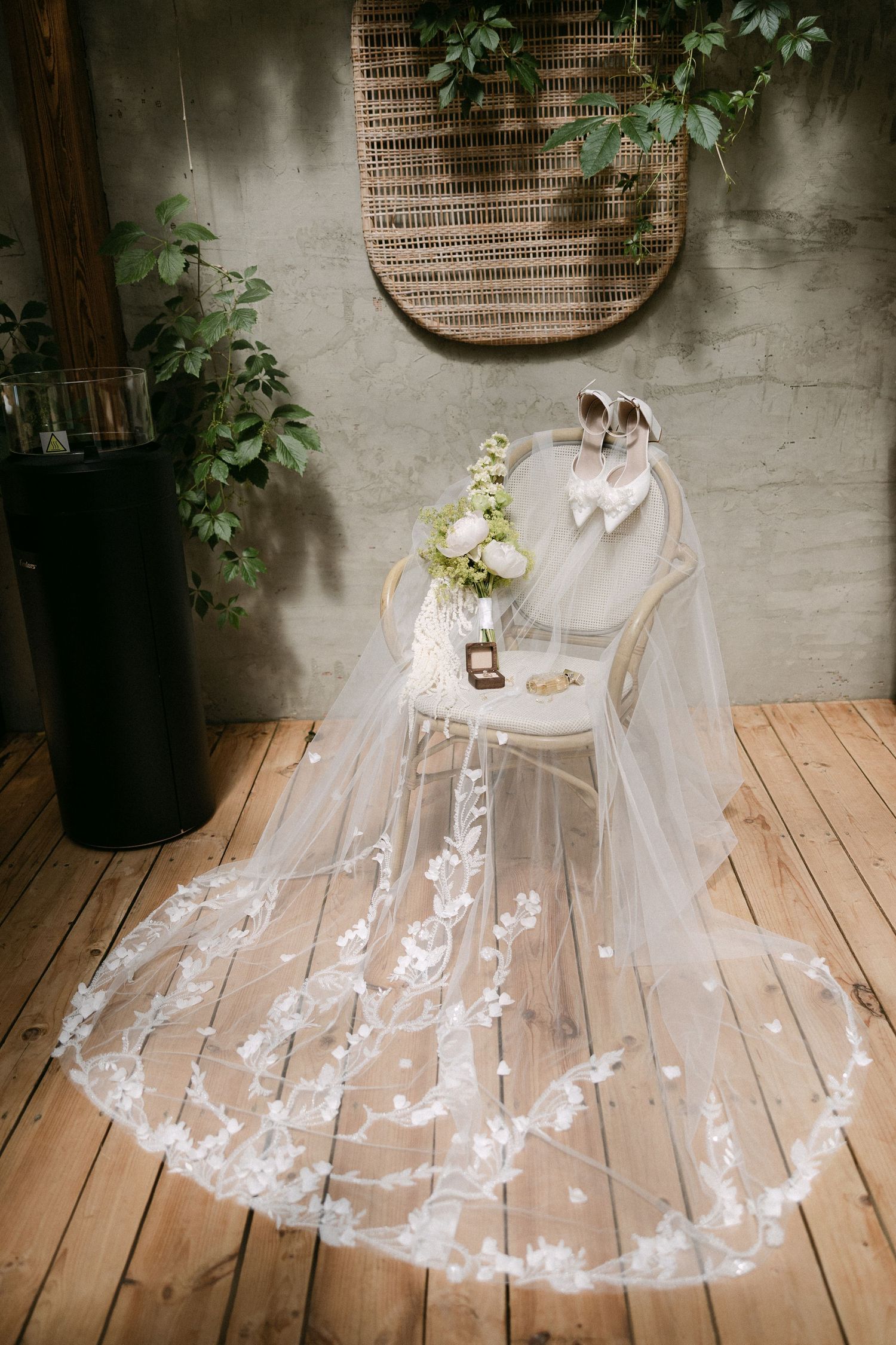 Elegant bridal veil with floral lace trim draped over a chair with wedding shoes and bouquet on wood floor.
