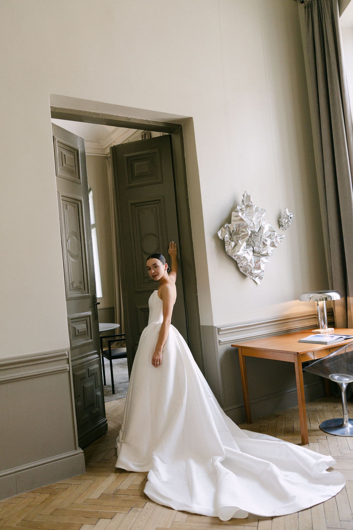 Bride in minimalist white ball gown with long train poses in classical European interior.
