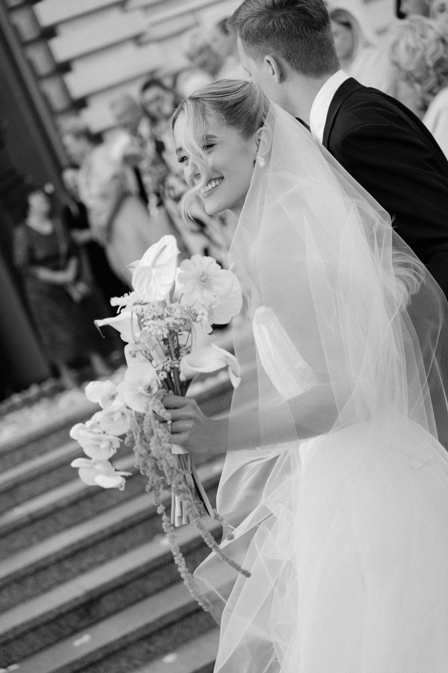 Radiant bride holding a floral bouquet smiles joyfully outside the church in a classic black and white photo.