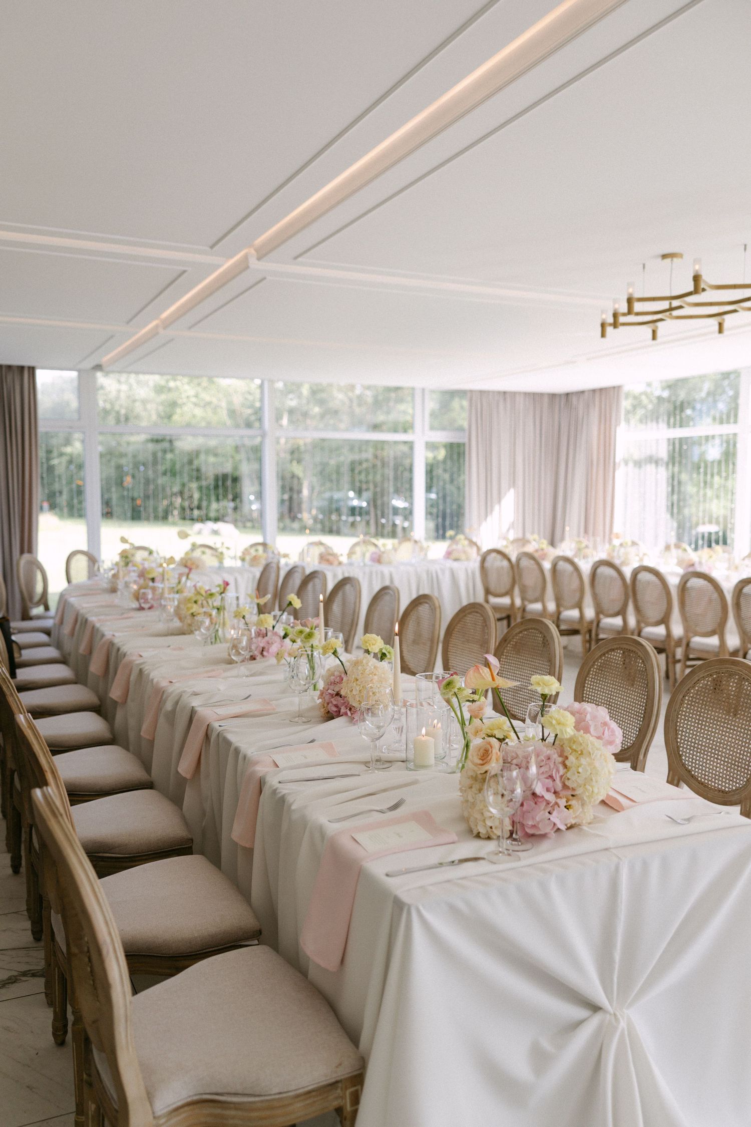Elegant wedding reception hall with long white tables, floral centerpieces, and gold chandelier.