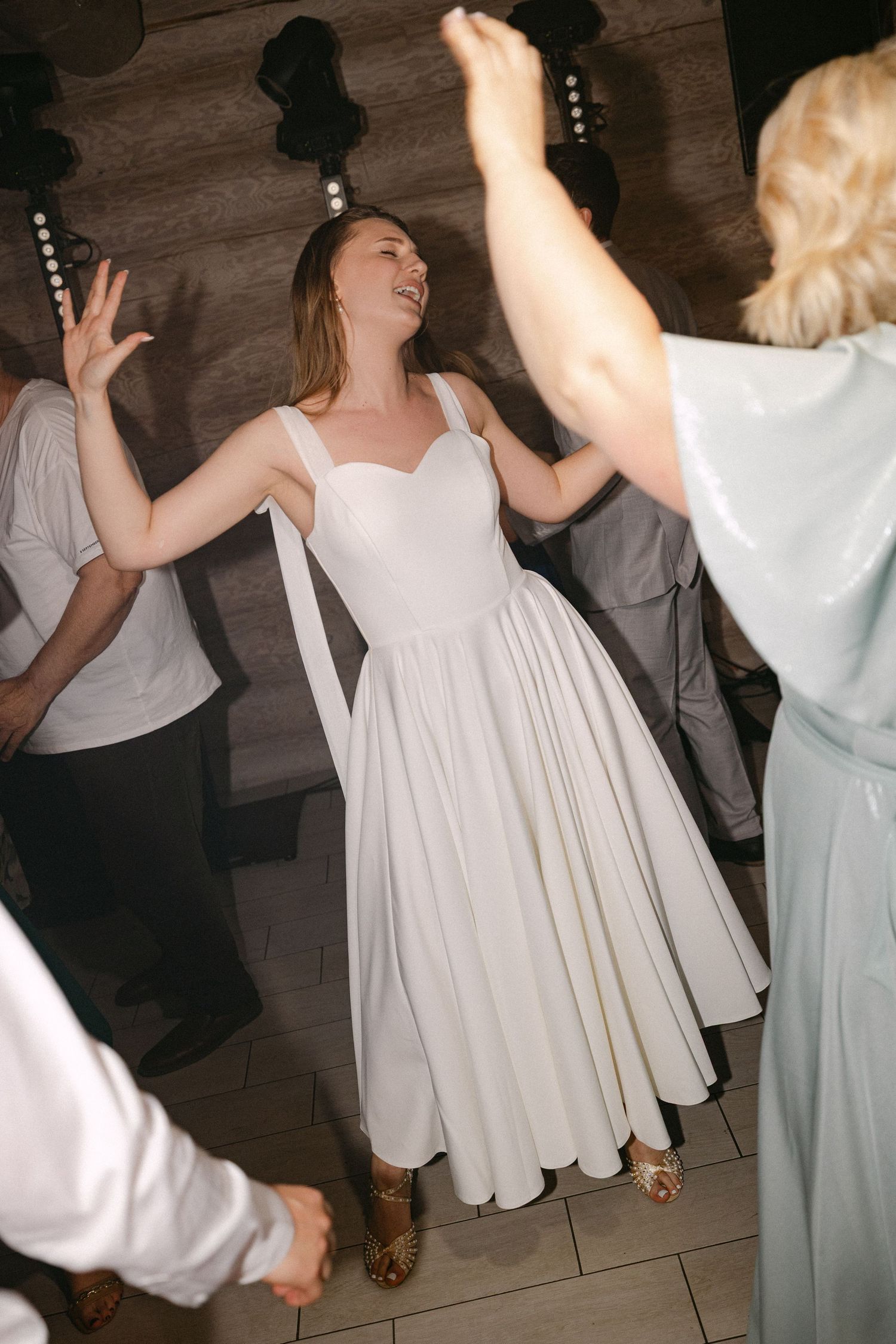Joyful bride in white tea-length dress dancing and laughing with guests at wedding reception party.