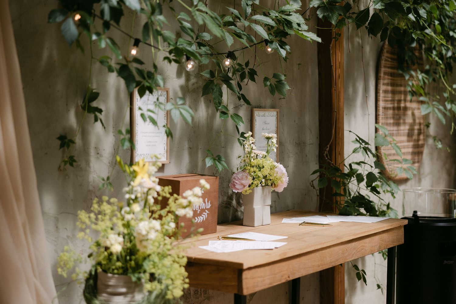 Rustic wooden welcome table with floral arrangements and string lights at an outdoor wedding venue.