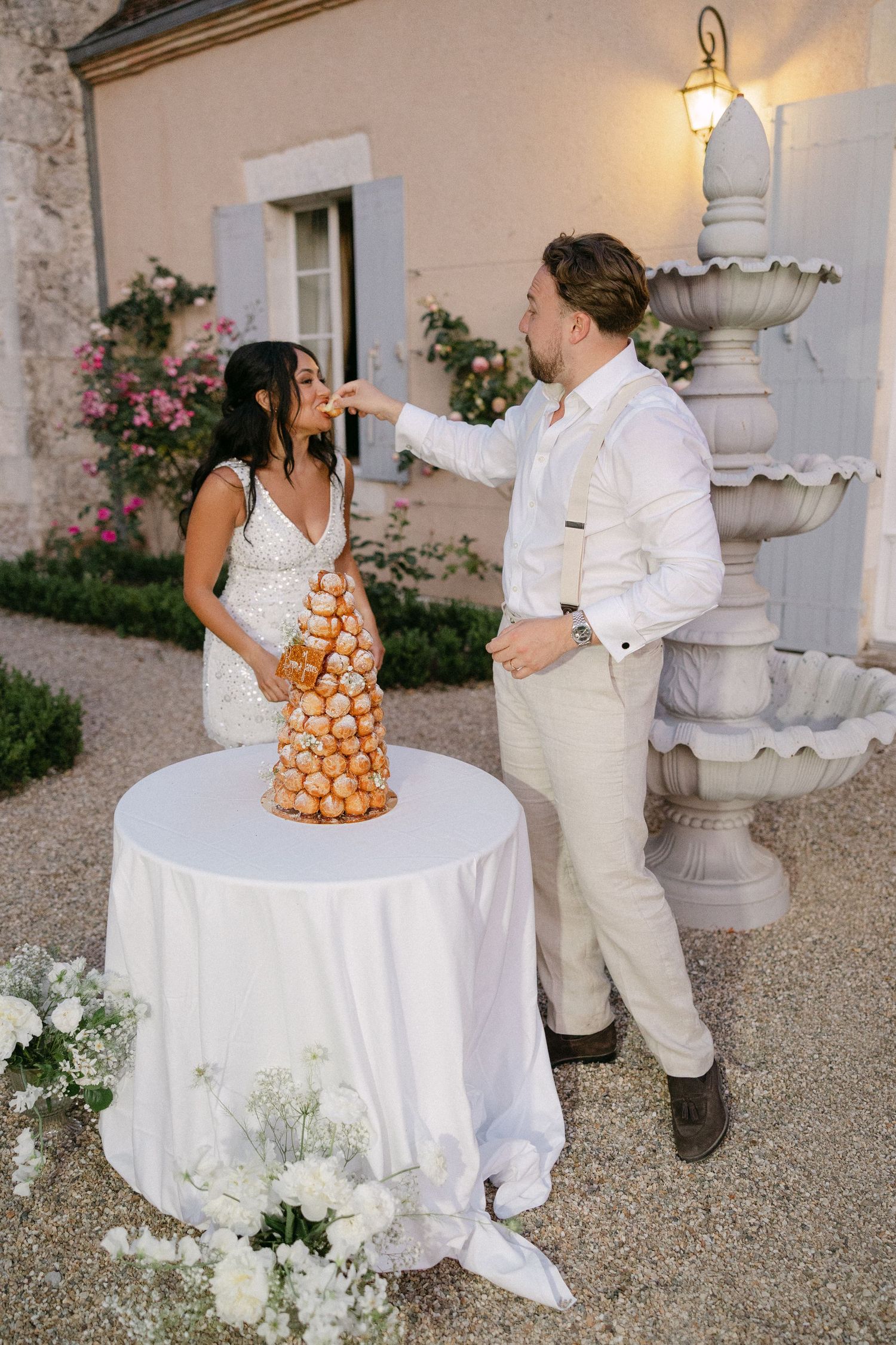 Bride and groom cutting a traditional French croquembouche wedding cake tower outdoors at a charming chateau venue.