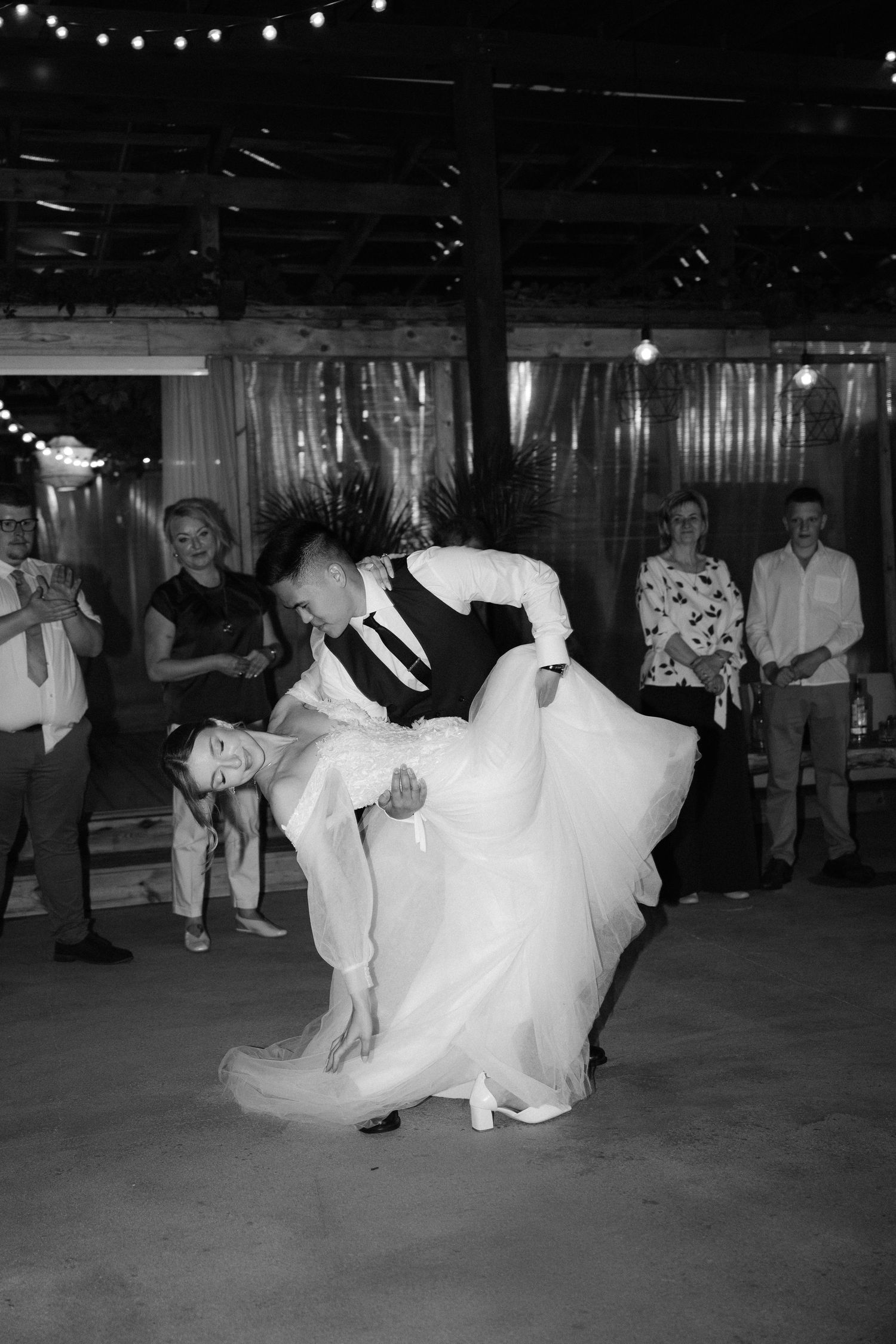 Black and white photo of groom dipping bride during first wedding dance.