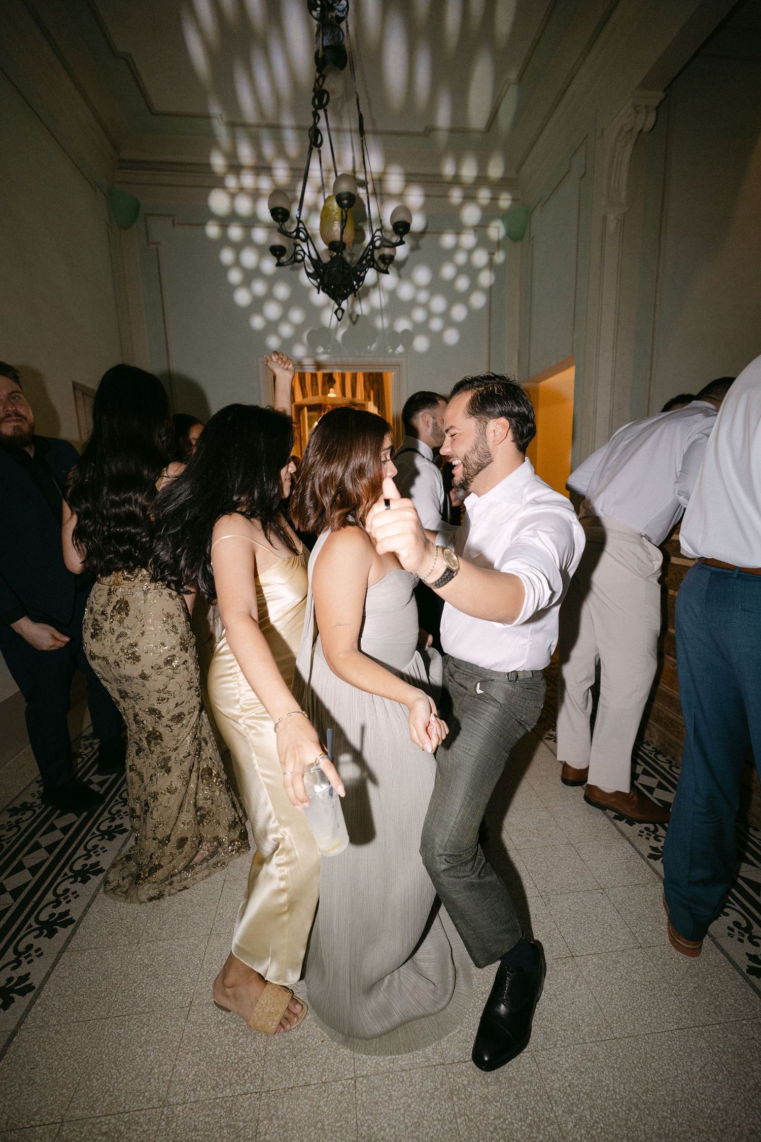 Guests dancing under chandelier with bokeh lights at elegant indoor wedding reception party.