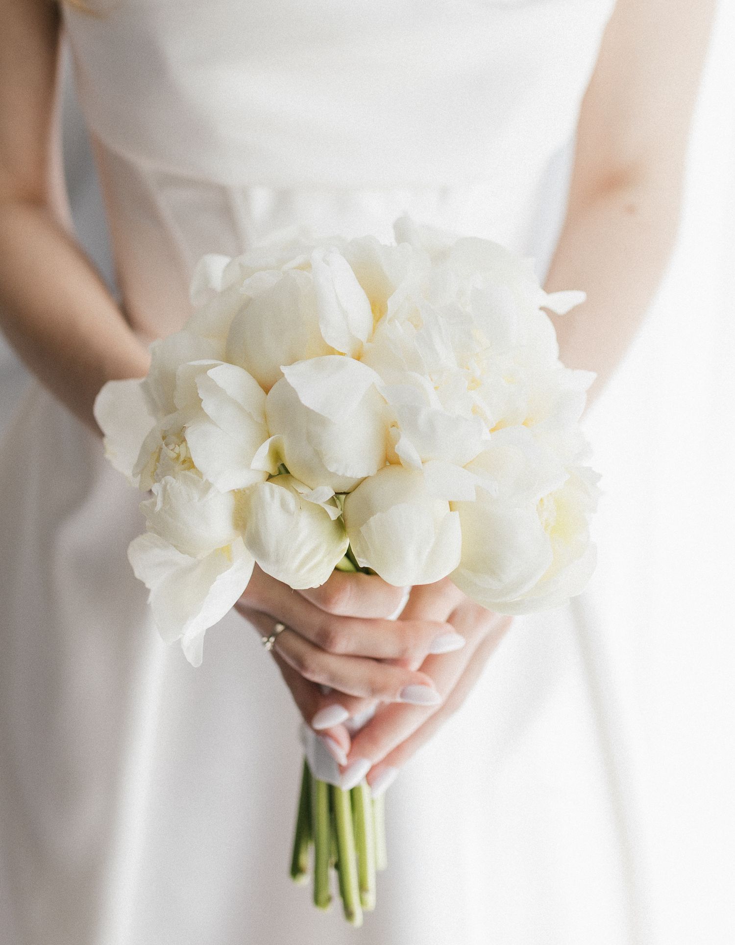 Elegant white orchid wedding bouquet held against a bright white background.