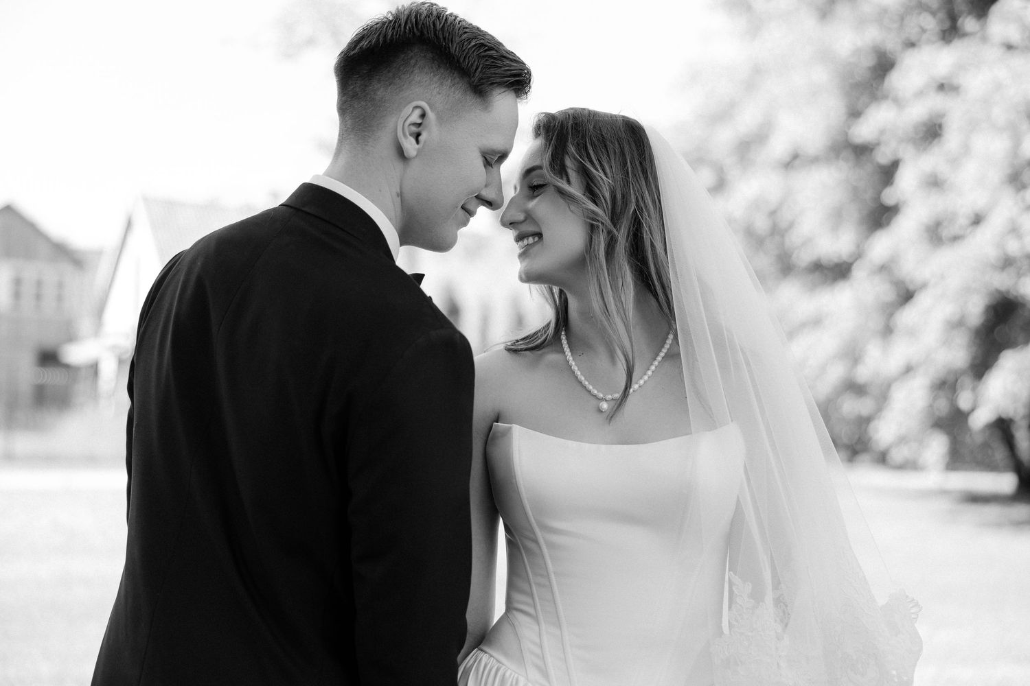 Black and white romantic portrait of newlywed couple gazing at each other outdoors on wedding day.