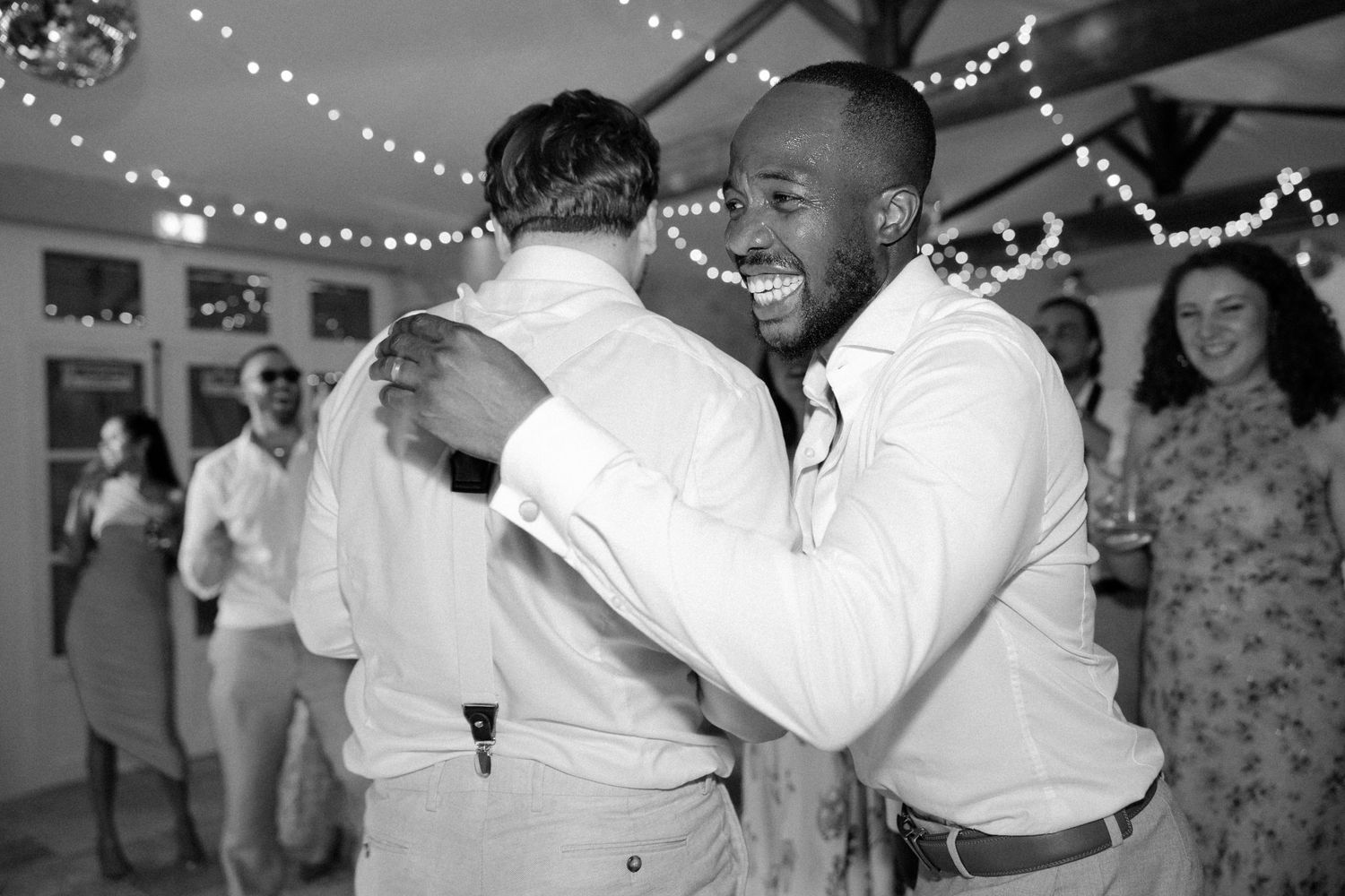 Black and white candid photo of two men sharing a warm embrace on the dance floor.