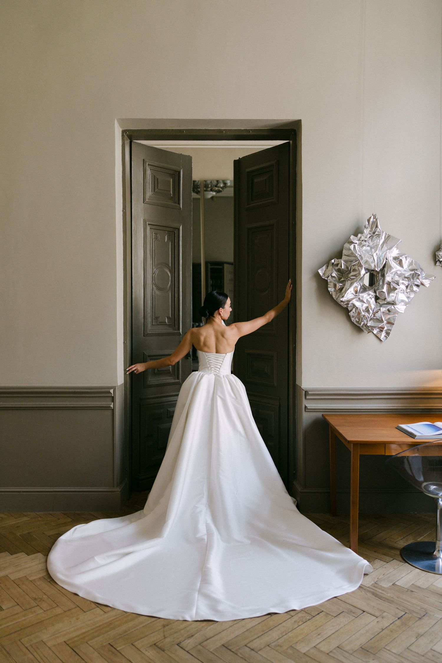 Bride in elegant white ballgown with long train viewed from behind opening ornate double doors.