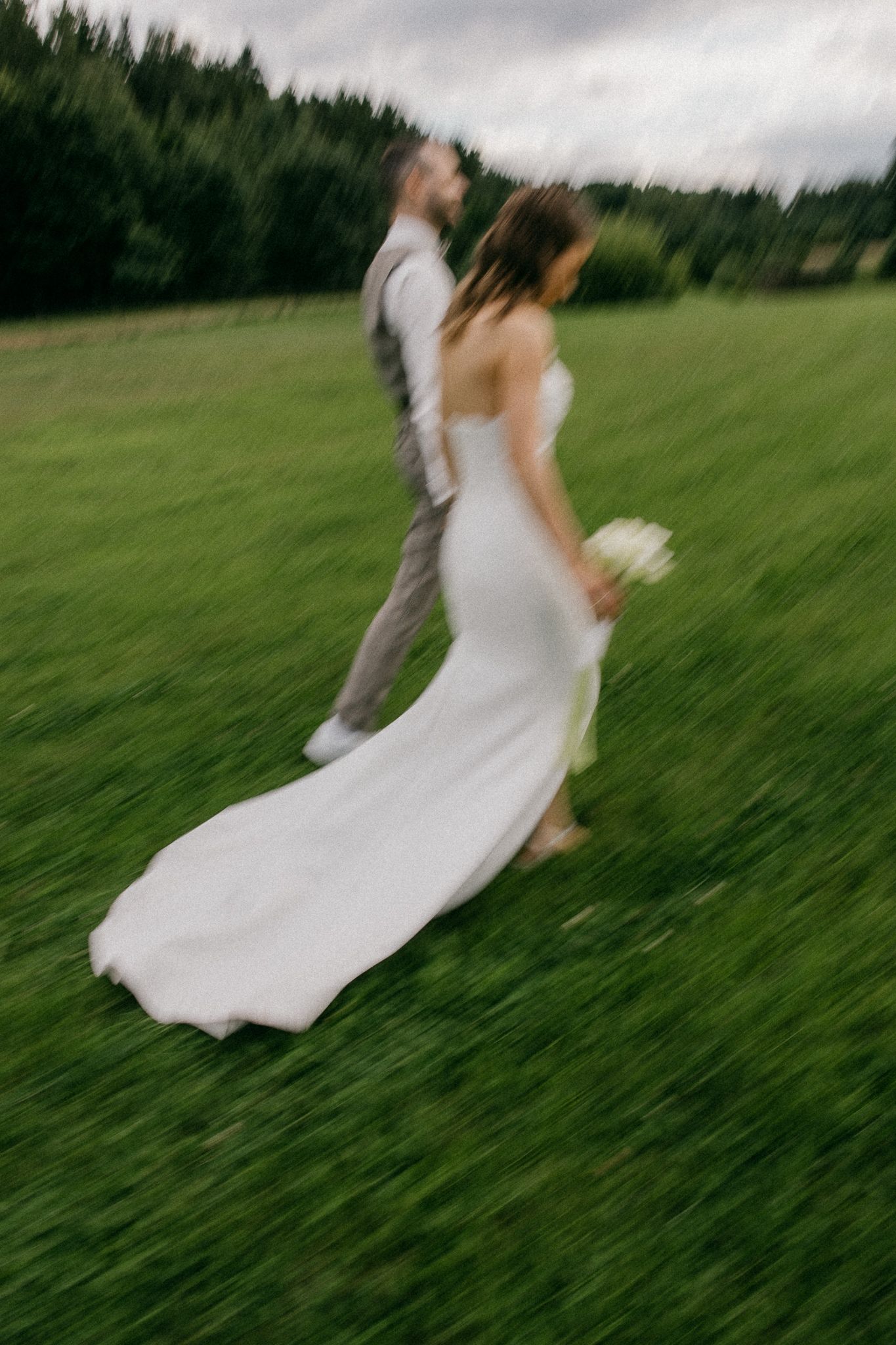 Dynamic shot of couple dancing on lush green hillside in wedding attire.
