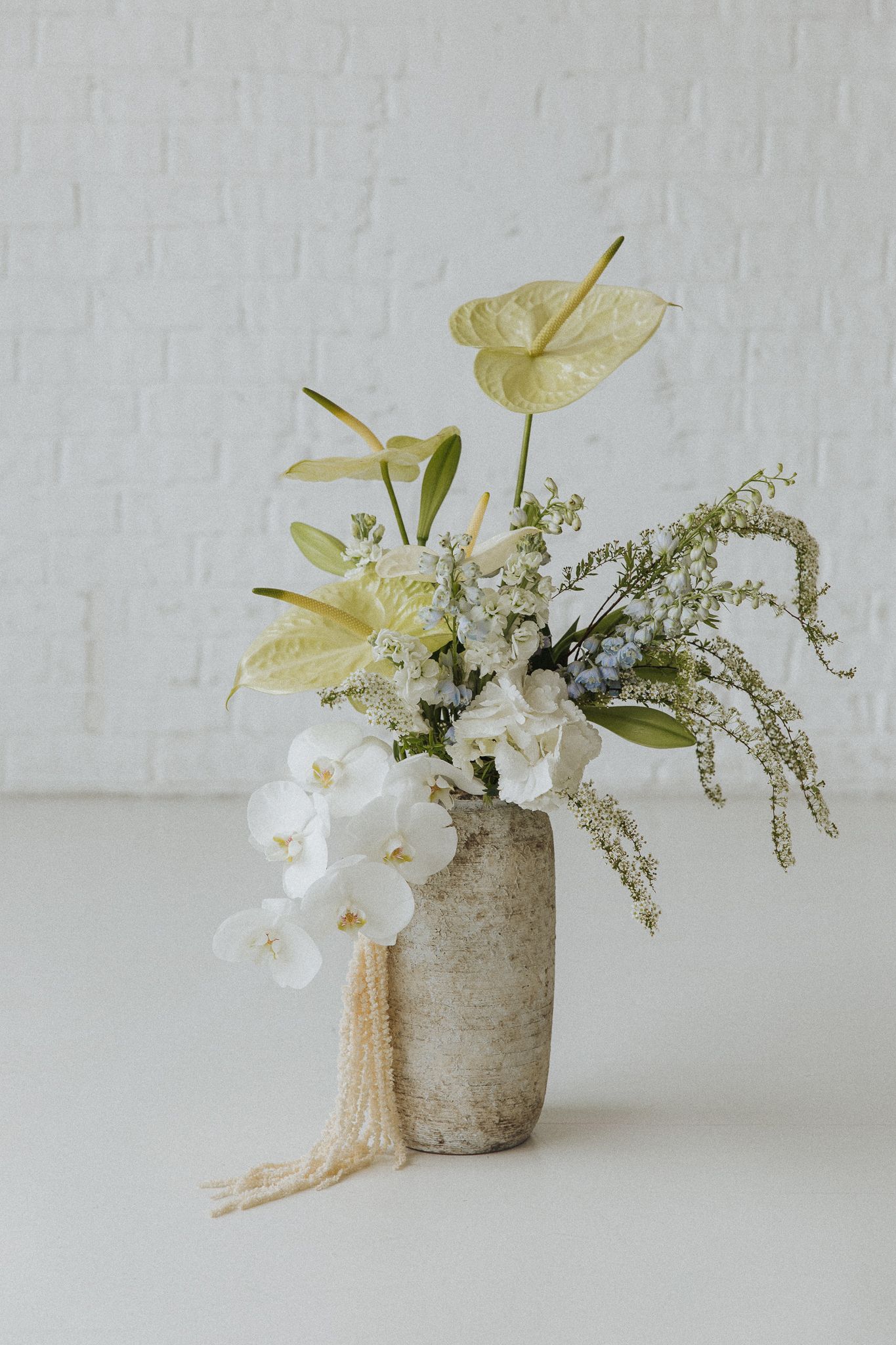 Modern floral arrangement with white orchids and yellow anthuriums in textured stone vases.