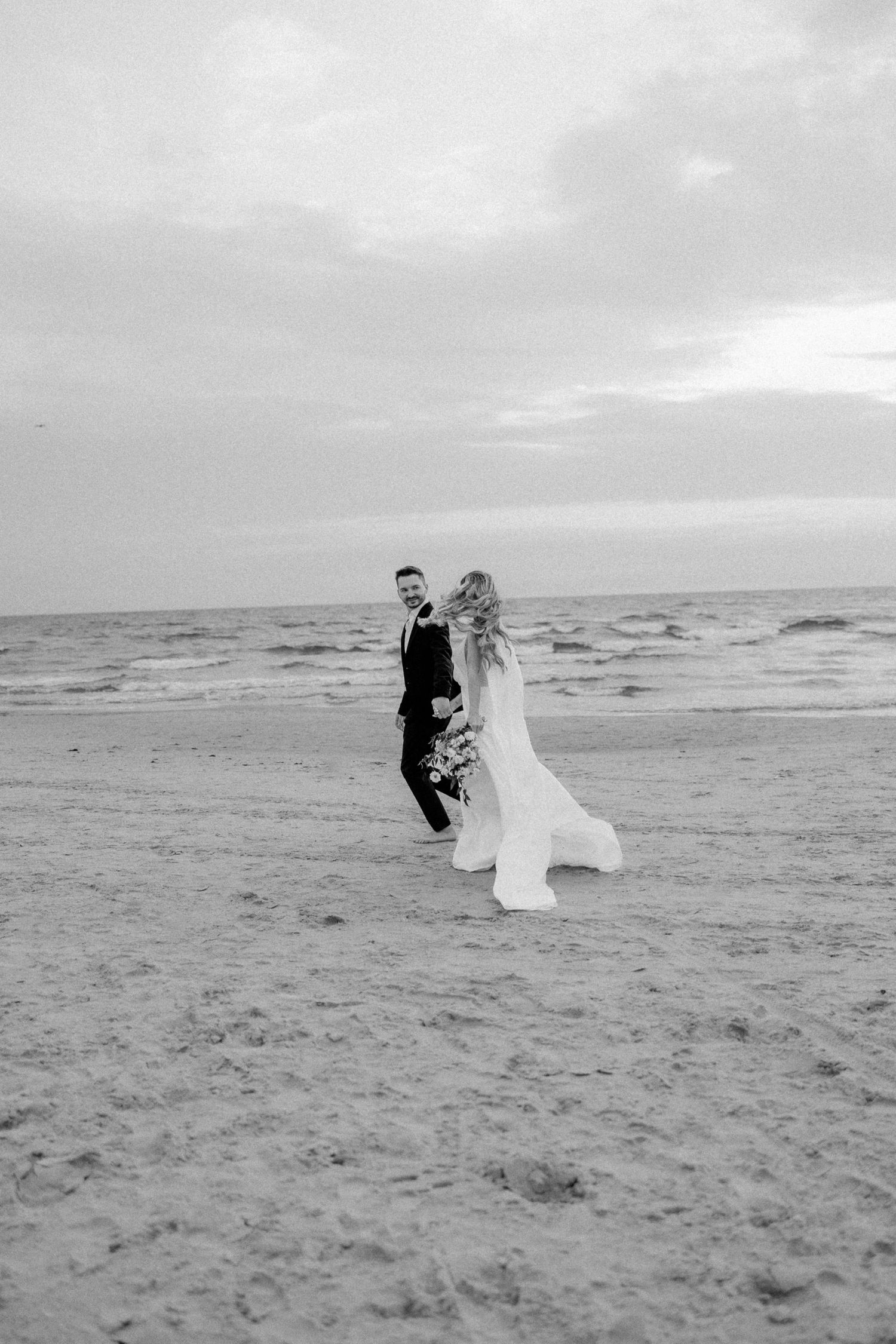 Wedding couple walking along a misty beach shore in black and white.