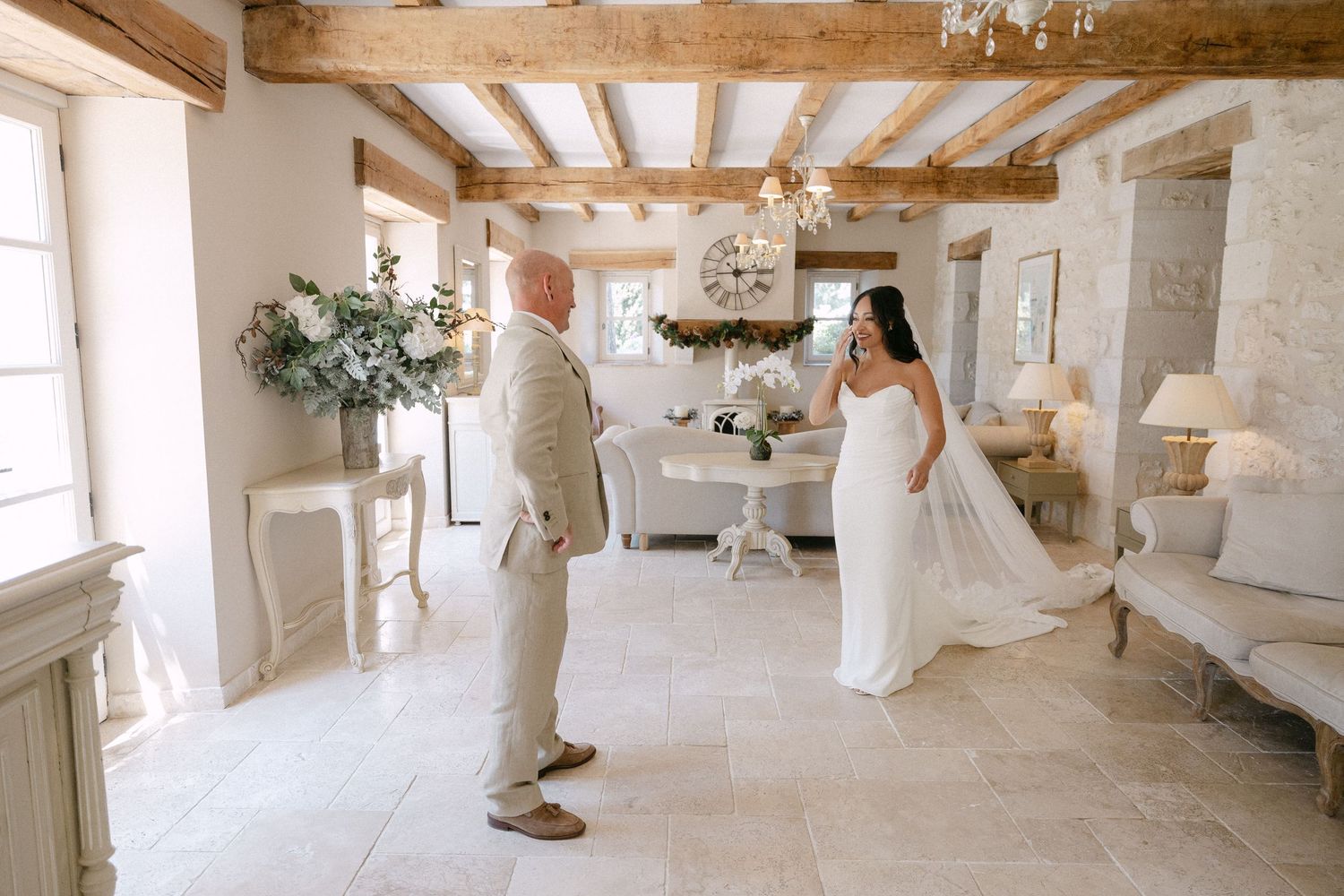 Bride in white gown shares first look moment with father in elegant French chateau interior with stone walls.