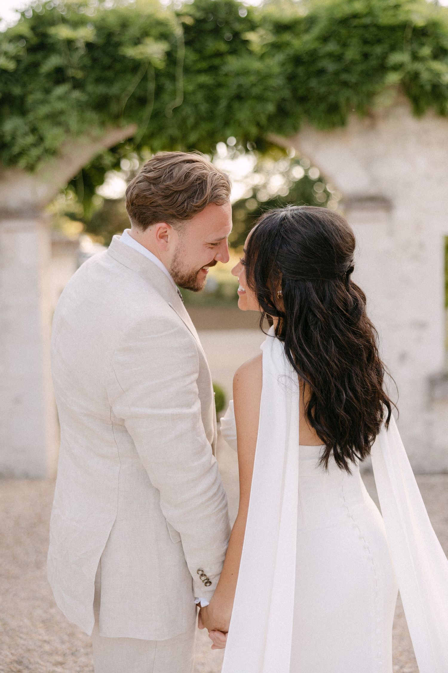 Bride and groom holding hands and sharing an intimate moment under a stone arch at sunset.