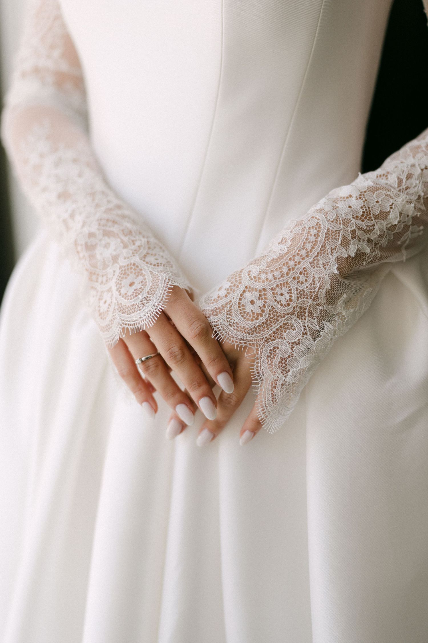 Bride in white wedding gown with elegant lace gloves, hands clasped showing diamond ring.
