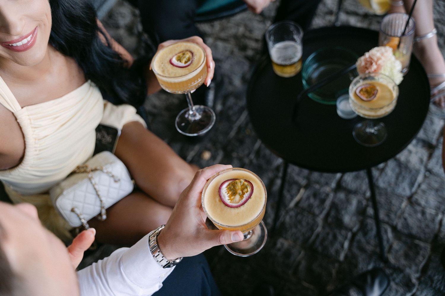 Guests enjoy passionfruit cocktails in coupe glasses at an outdoor wedding reception gathering.