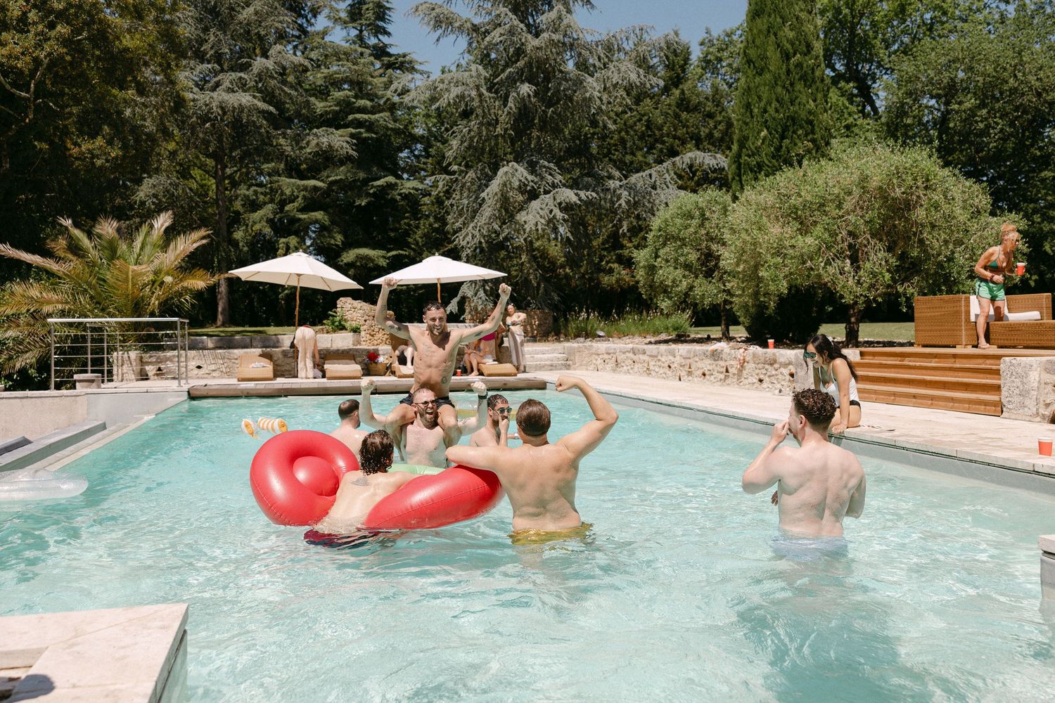 Wedding guests enjoying a sunny pool party with a red inflatable float at a French estate.