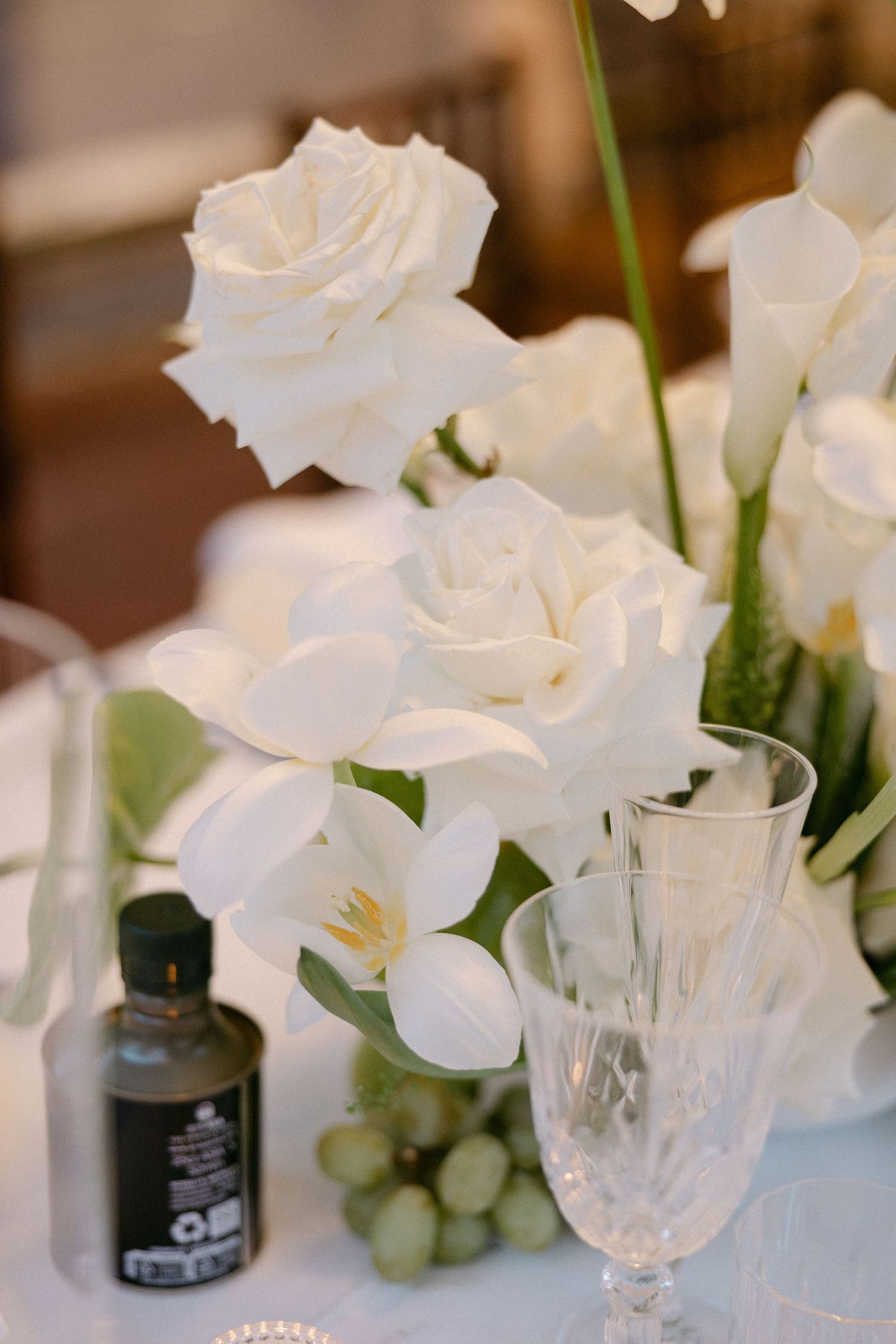 White roses, calla lilies, and orchids surround a crystal glass and grapes at wedding reception.