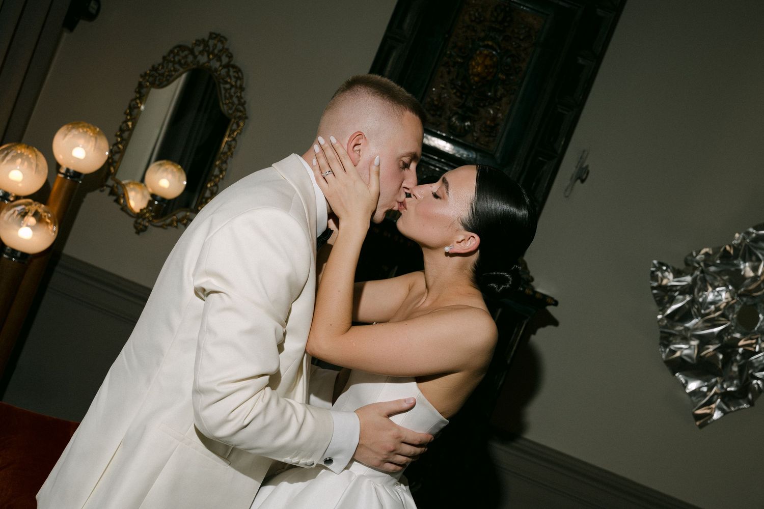Bride and groom share a romantic kiss at their wedding reception in an elegant venue.
