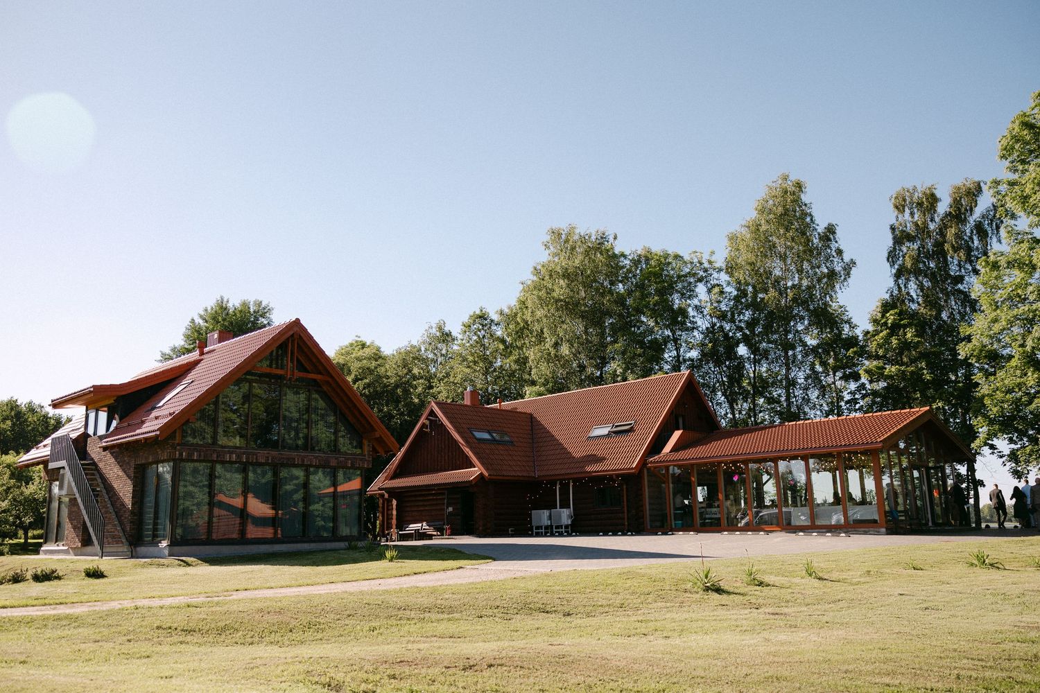 Rustic red-roofed wedding venue surrounded by green trees under clear blue sky.