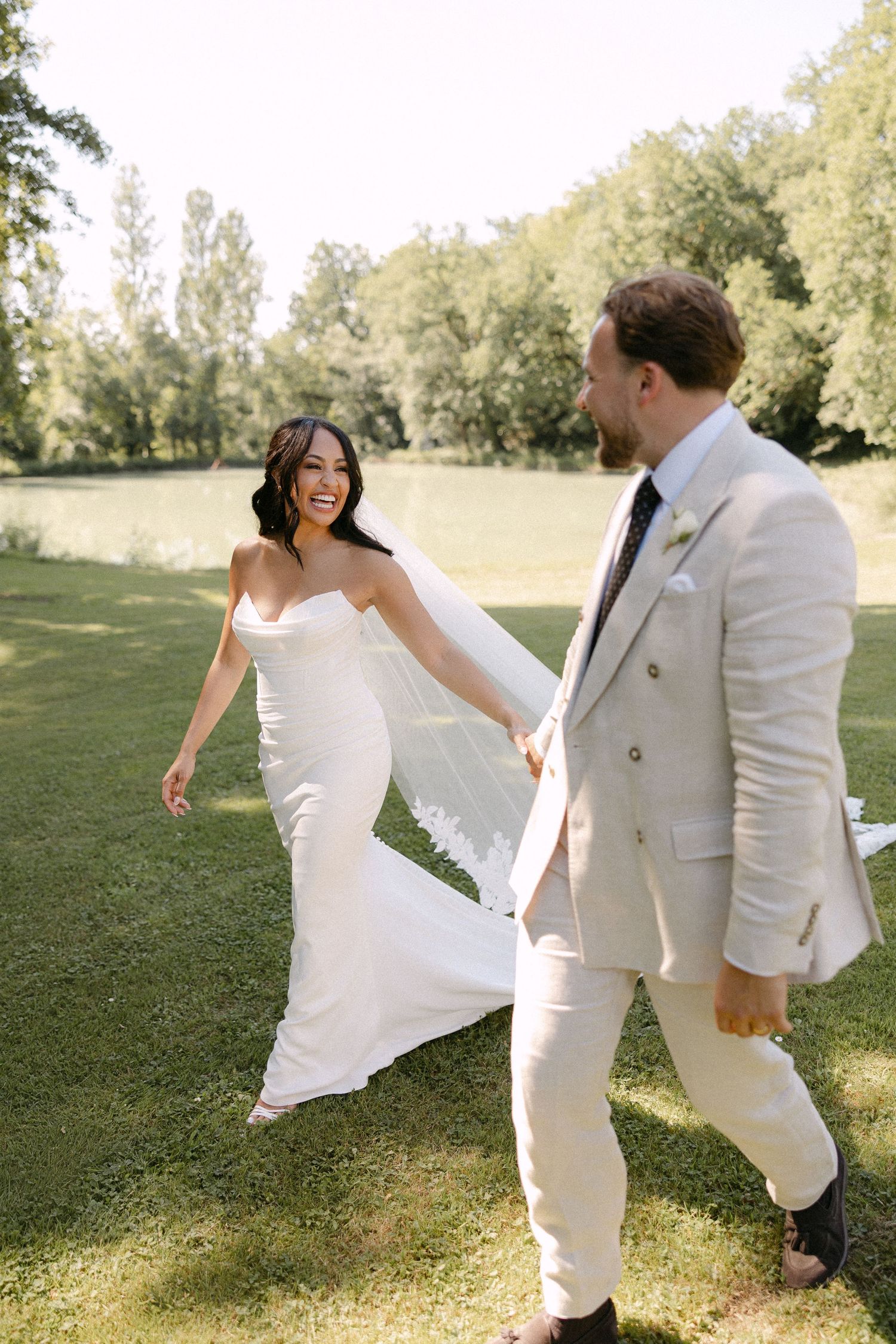 Happy bride and groom walking hand in hand across green lawn on sunny wedding day.
