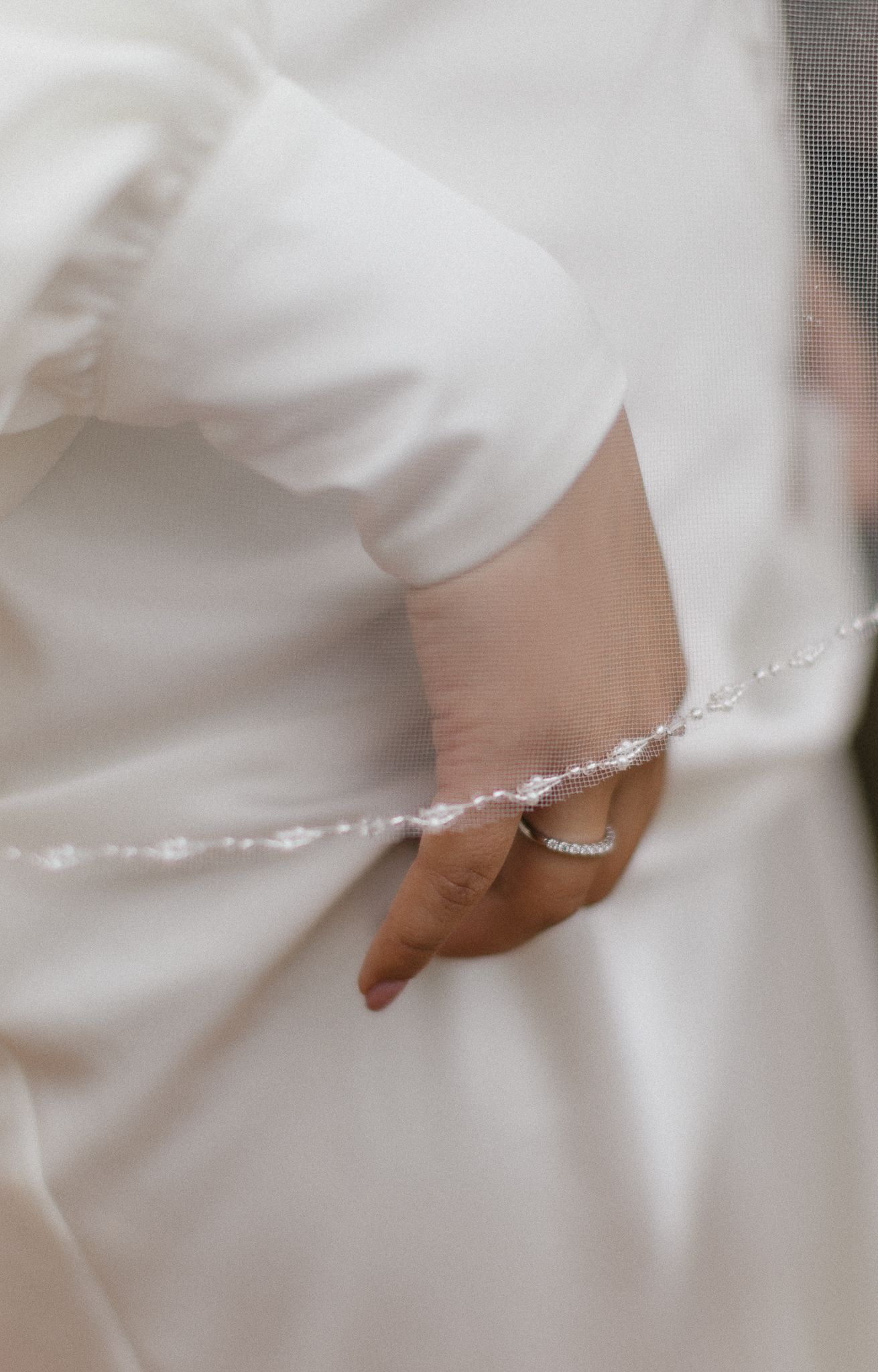 Close-up view of a delicate pearl bracelet adorning a wrist against a white dress fabric background.