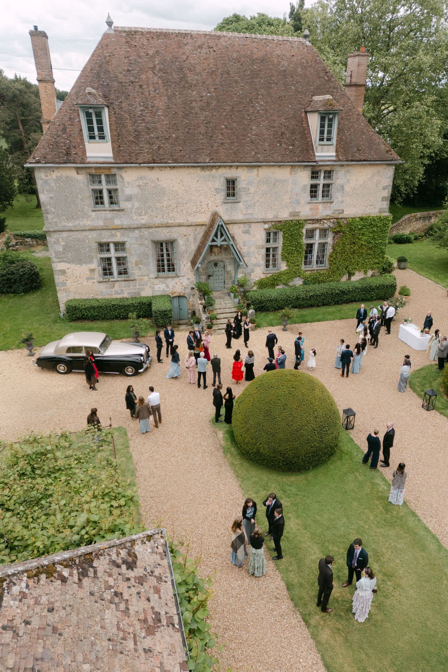 Aerial view of guests mingling outside a grand French chateau during an elegant wedding reception.